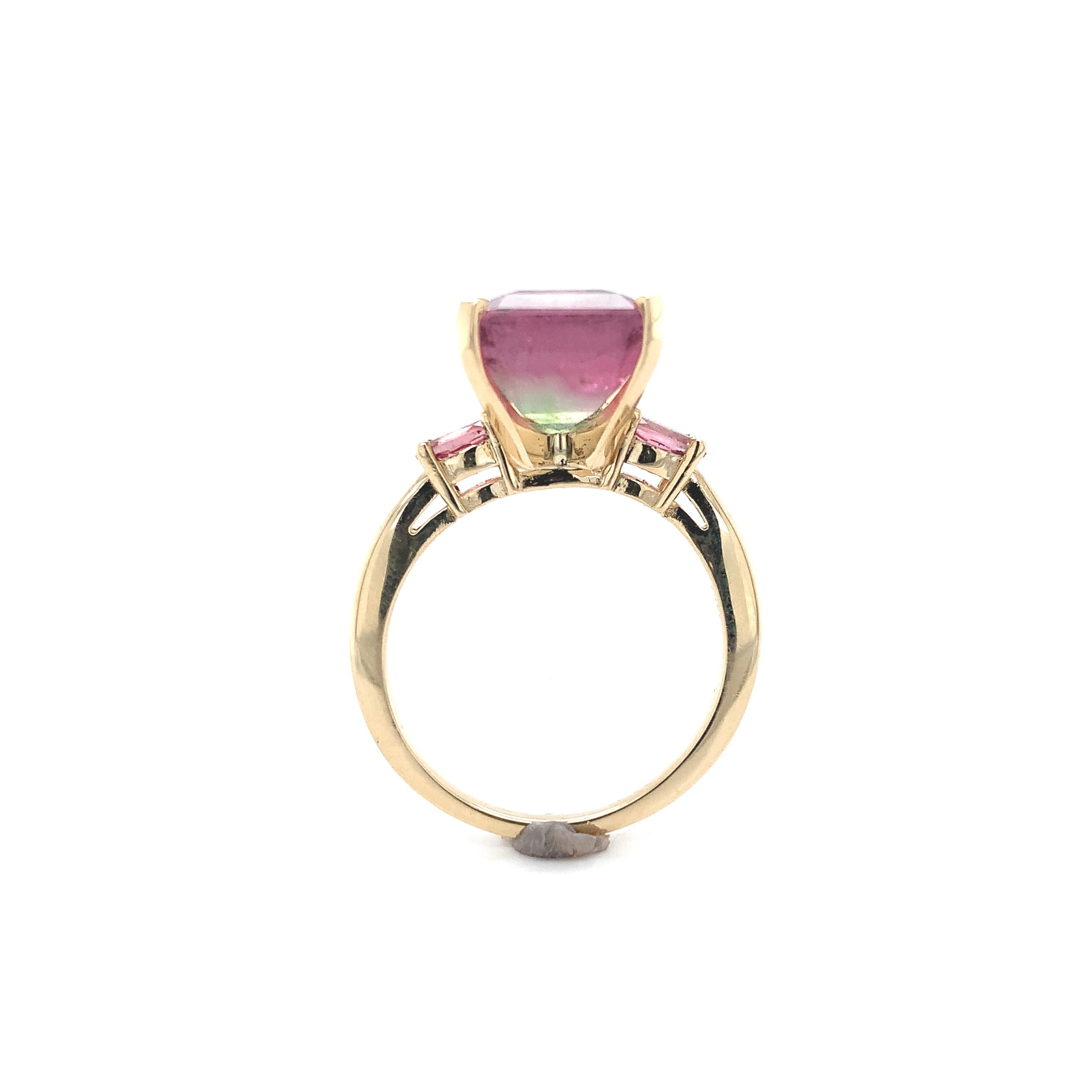 A 14K yellow gold ring featuring a bi-color watermelon tourmaline weighing 6.71 carats. The tourmaline has color from pink to clear to light sea green. The tourmaline is an emerald cut and measures about 11mm x 9mm. There are 2 oval pink tourmaline