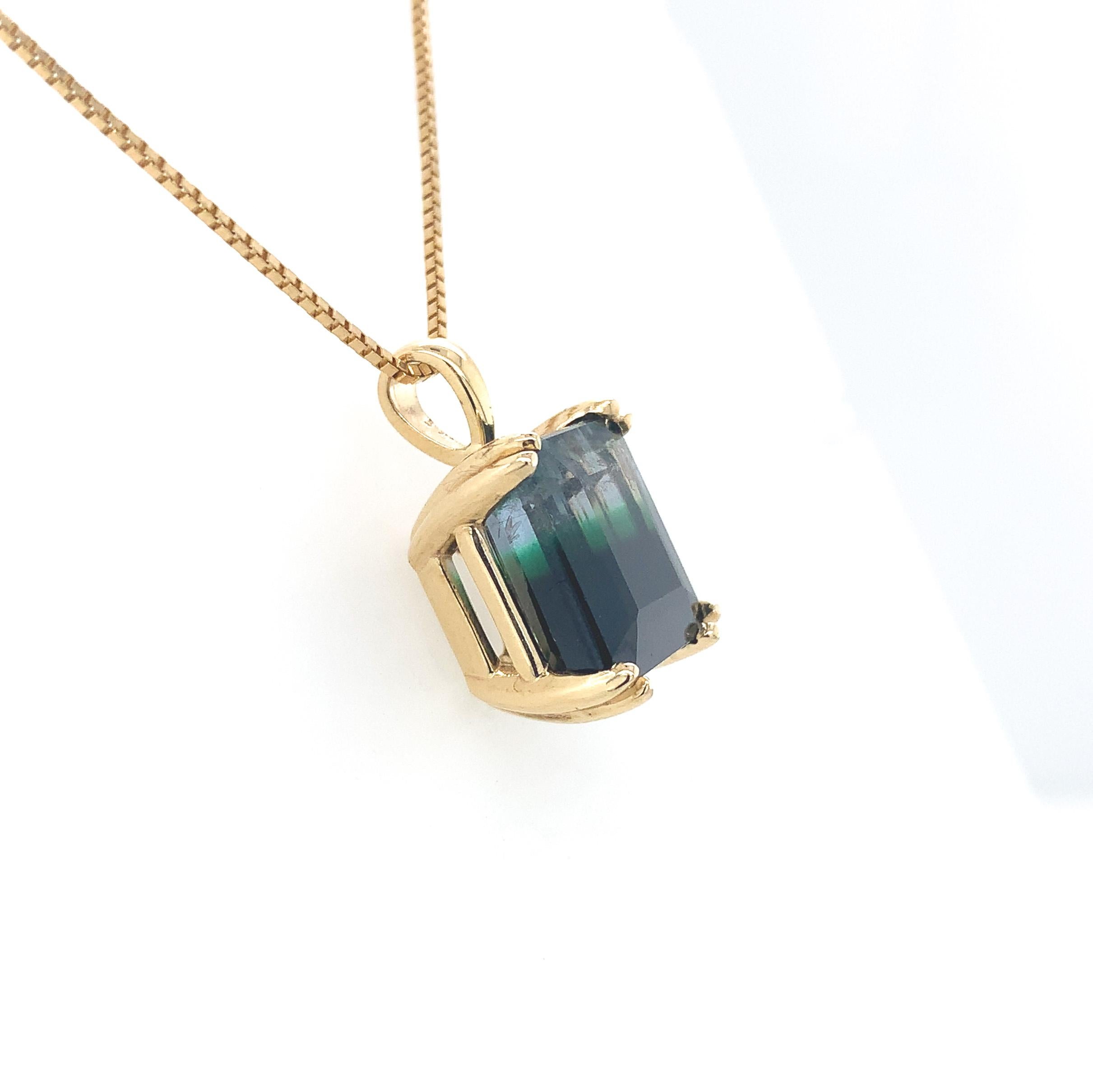 14K yellow gold pendant featuring a bi-color tourmaline weighing 7.92 carats. The tourmaline has color from clear to green to very dark green, almost black. The emerald cut tourmaline measures about 11.5mm x 10mm. The tourmaline is set in a