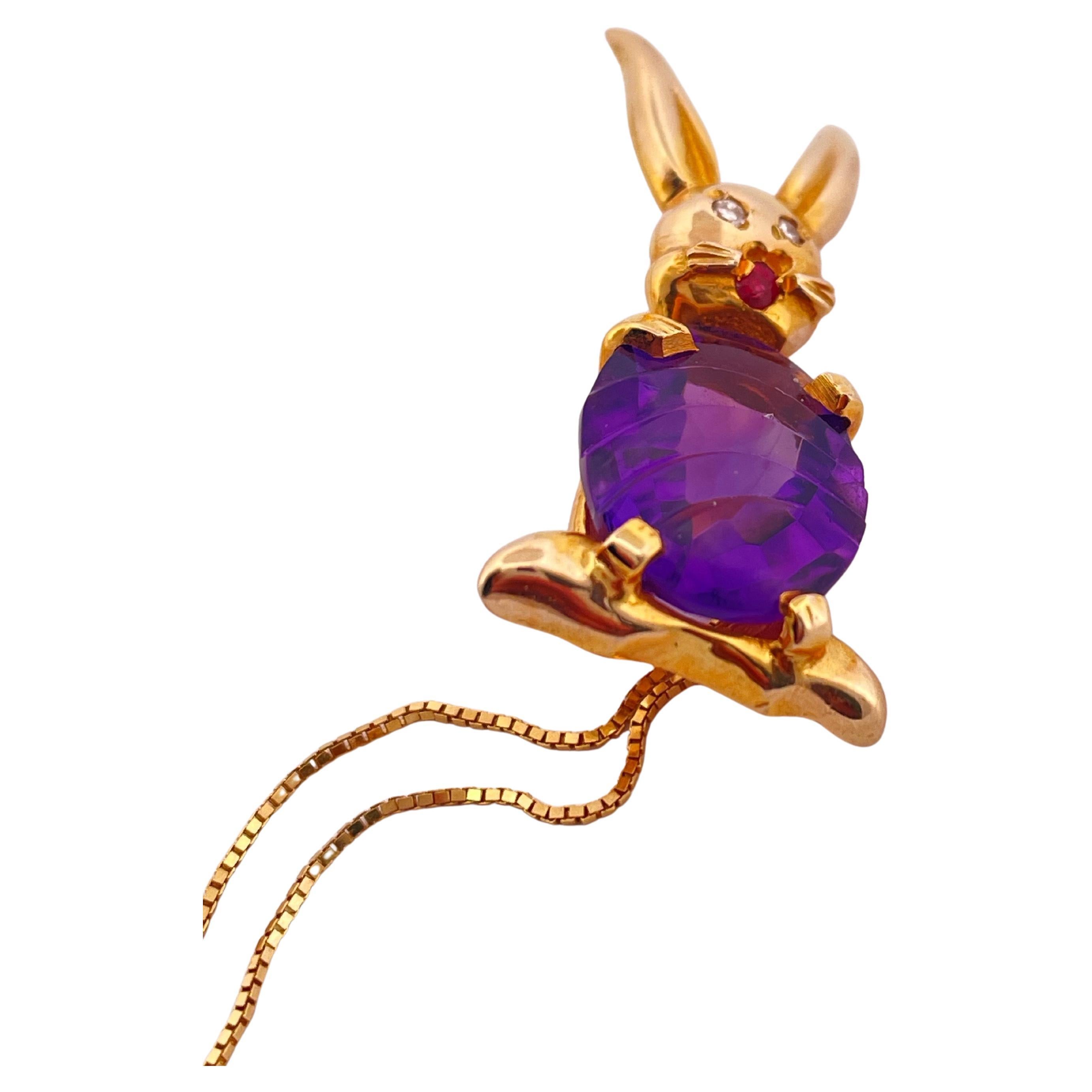 Un fascino stravagante incontra l'artigianato in questo delizioso ciondolo e catena in oro giallo 14k. Sapientemente realizzato a forma di coniglietto giocoso, il ciondolo presenta un'ametista riccamente colorata e finemente sfaccettata, intagliata