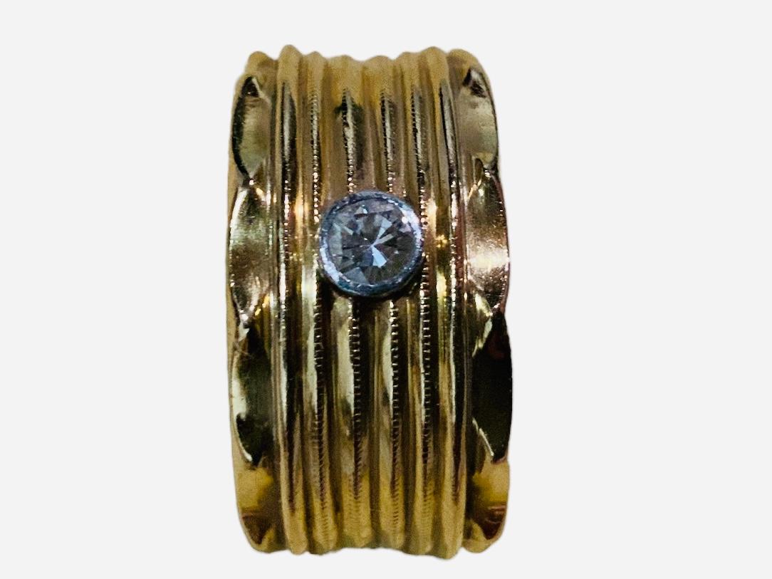 Il s'agit d'une bague en or jaune 14K et diamants. L'anneau représente une large bande nervurée avec un seul diamant rond étincelant dans un chaton en or au centre. Son poids est de 7 grammes ou 4,5 dwt.