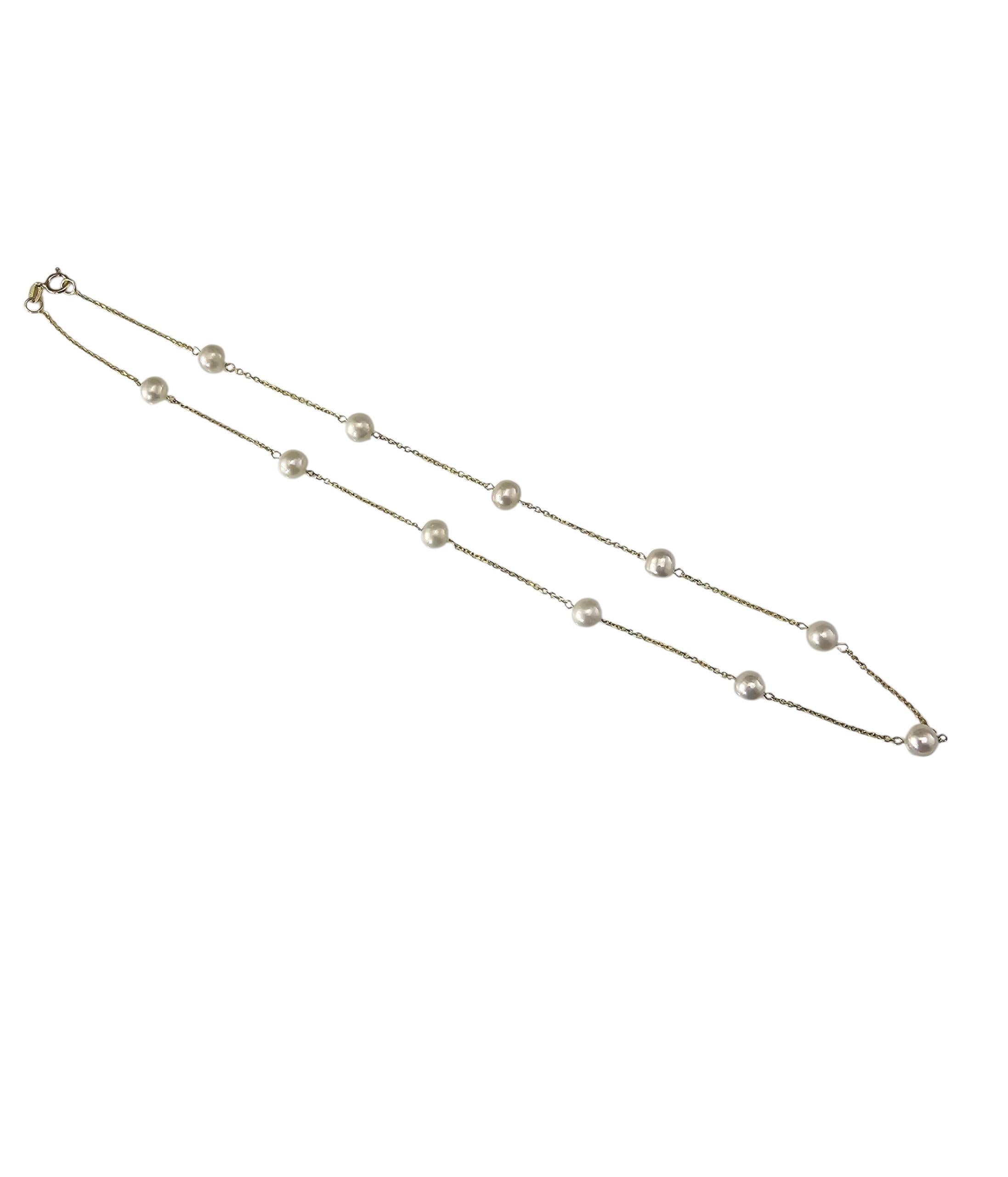 Collier station en or jaune 14K et perles-

Ce délicat collier station présente 11 perles blanches rondes (6 mm chacune) régulièrement espacées sur une fine chaîne en or jaune 14 carats, donnant un aspect flottant et sans effort. Une pièce