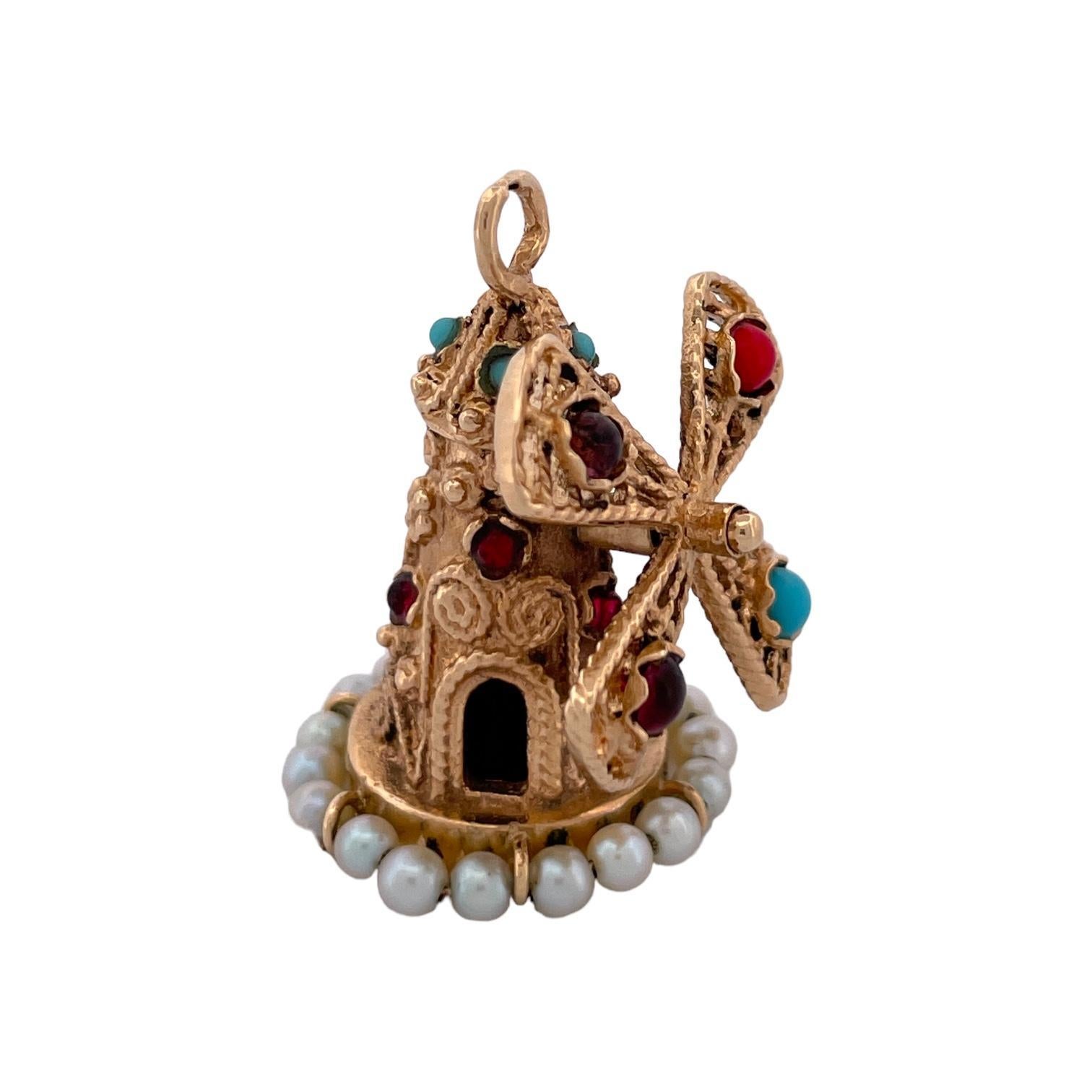 Un charme distinctif, ce pendentif en forme de moulin à vent complexe est fabriqué en métal doré orné. Orné de pierres rouges et turquoises vibrantes, il présente de délicates lames ajourées. Une rangée de petites perles entoure la base, ajoutant de