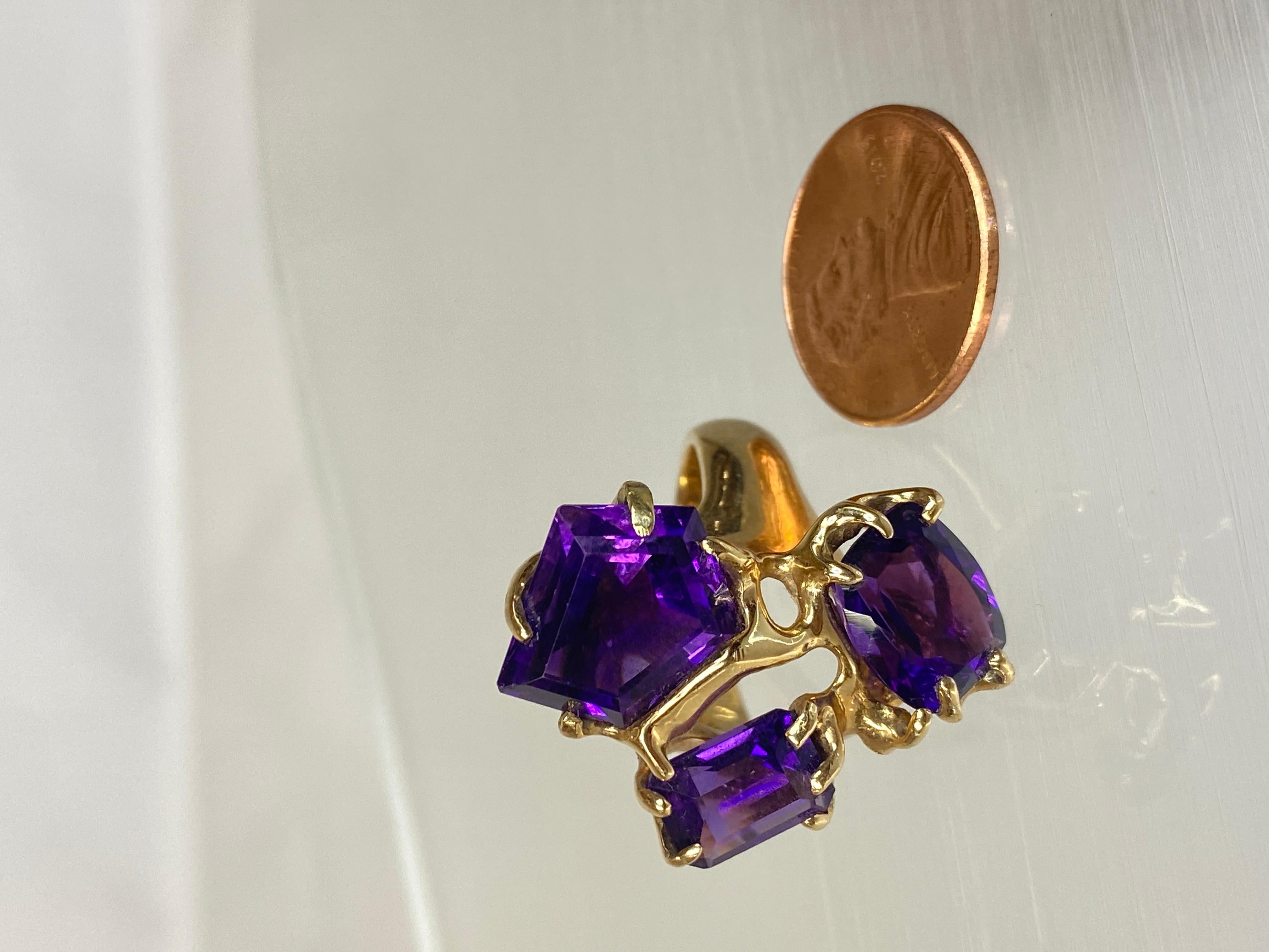 An ultra-modern 14K yellow gold cocktail ring with three large asymmetrical amethyst gemstones is a striking statement piece that epitomizes contemporary elegance and bold design. Crafted with sleek lines and avant-garde flair, this ring captures