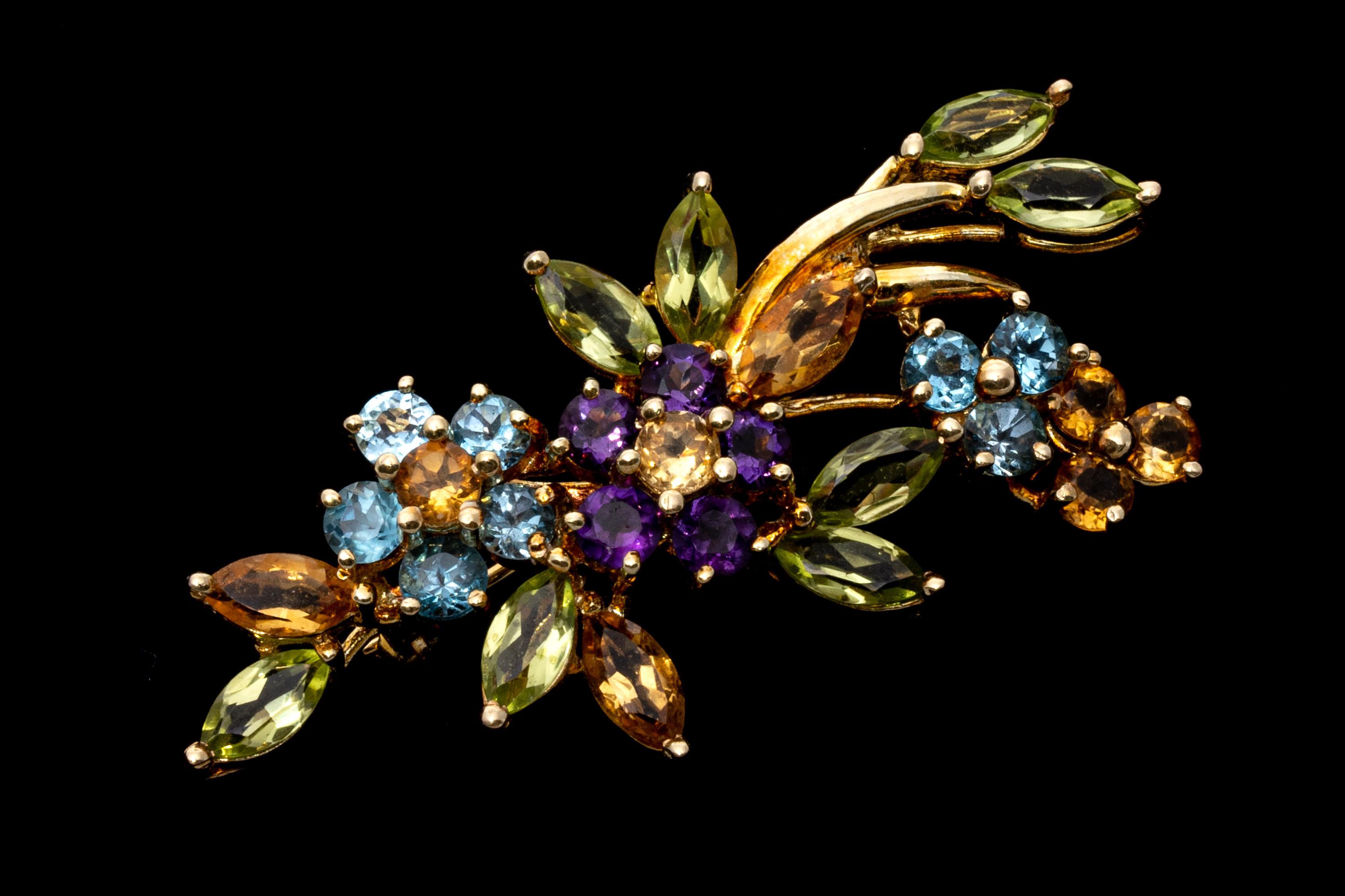 14k yellow brooch. This striking pin contains a collection of marquise and round faceted colored stones, set into a beautiful spray of flowers and leaves. The stones include medium blue color blue topaz (approximately 0.56 TCW), chartreuse green