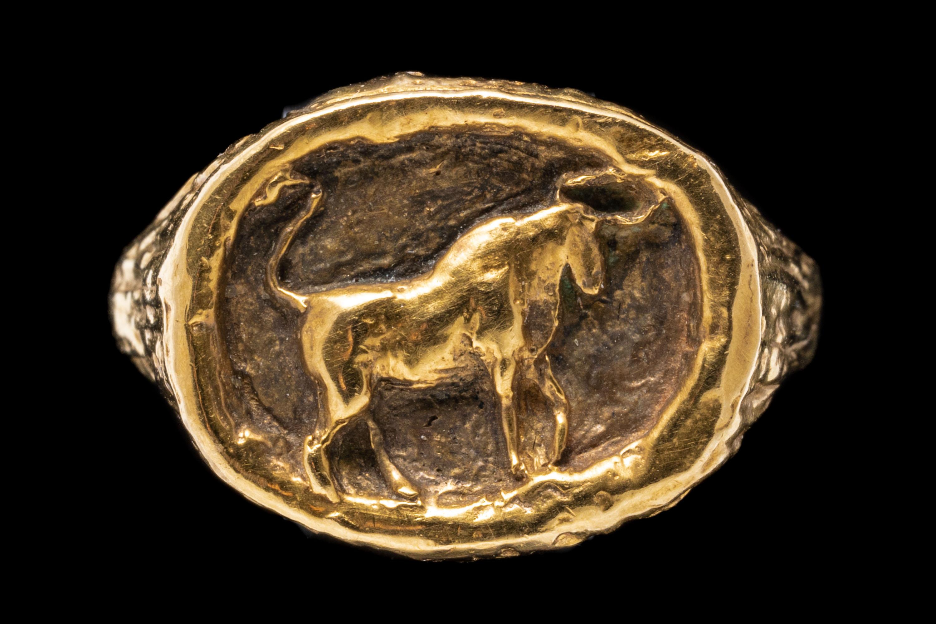 14k yellow gold ring. This unusual yellow gold ring has a blackened horizontal oval center, decorated with a high polished Taurus bull motif, edged with a wood grain style gallery.
Marks: 14k
Dimensions: 9/16