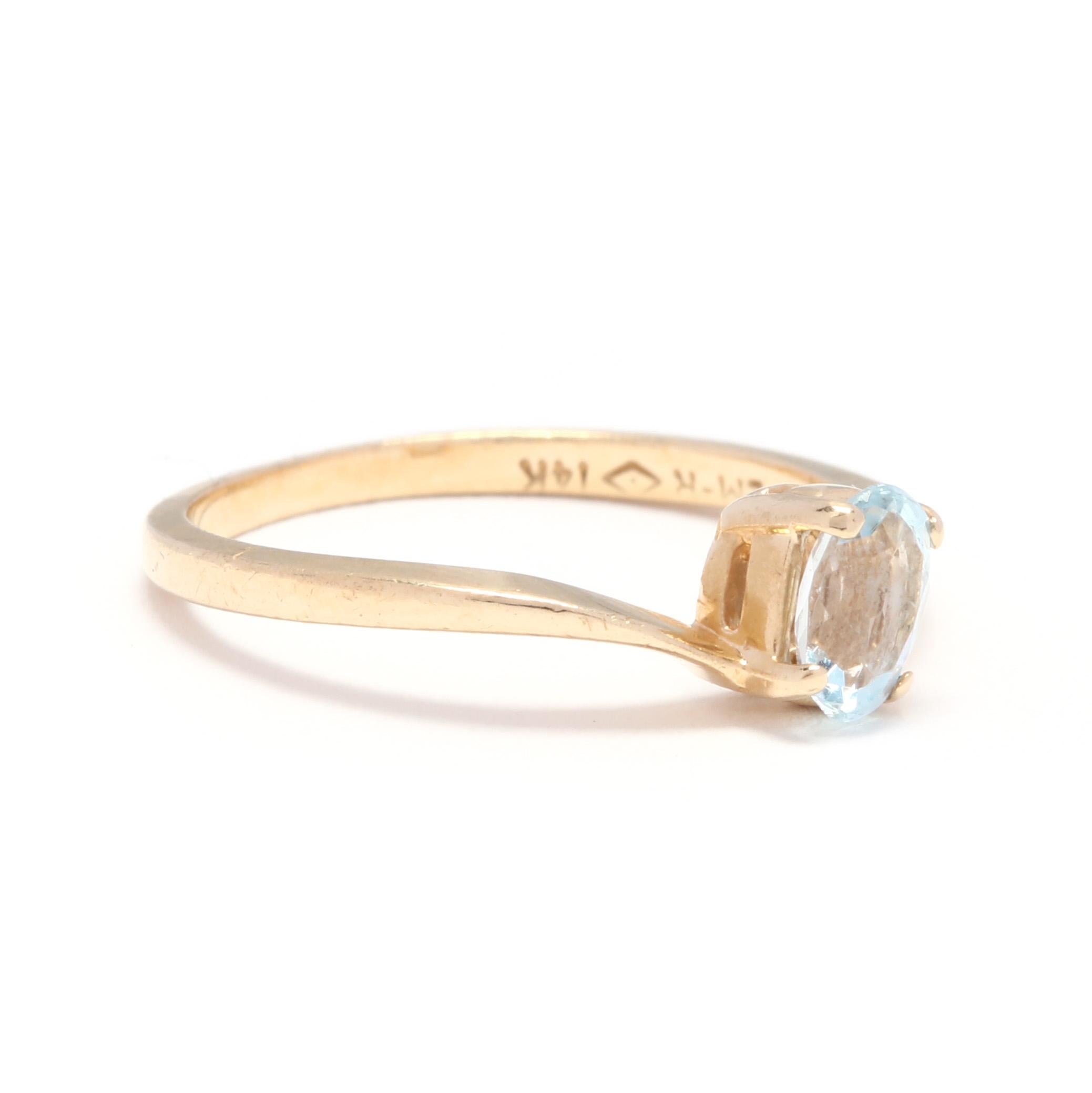 A 14 karat yellow gold and blue topaz bypass ring solitaire ring. This ring features a prong set, oval cut blue topaz stone set in a bypass mounting and with a slightly tapered shank.

Stone:
- blue topaz
- oval cut, 1 stone
- 6 x 4 mm

Ring Size