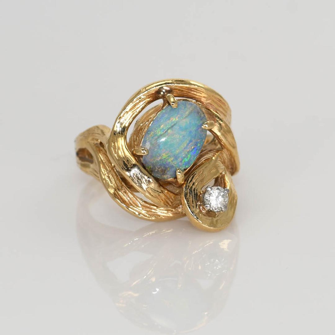 Bague pour femme en or jaune 14k, de forme libre, ornée d'opales et de diamants.
Estampillé 14k et pèse 9,9 grammes.
L'opale de roche australienne présente un jeu de couleurs bleu, vert et un peu de rouge.
Sur le pourtour et au dos de l'opale se