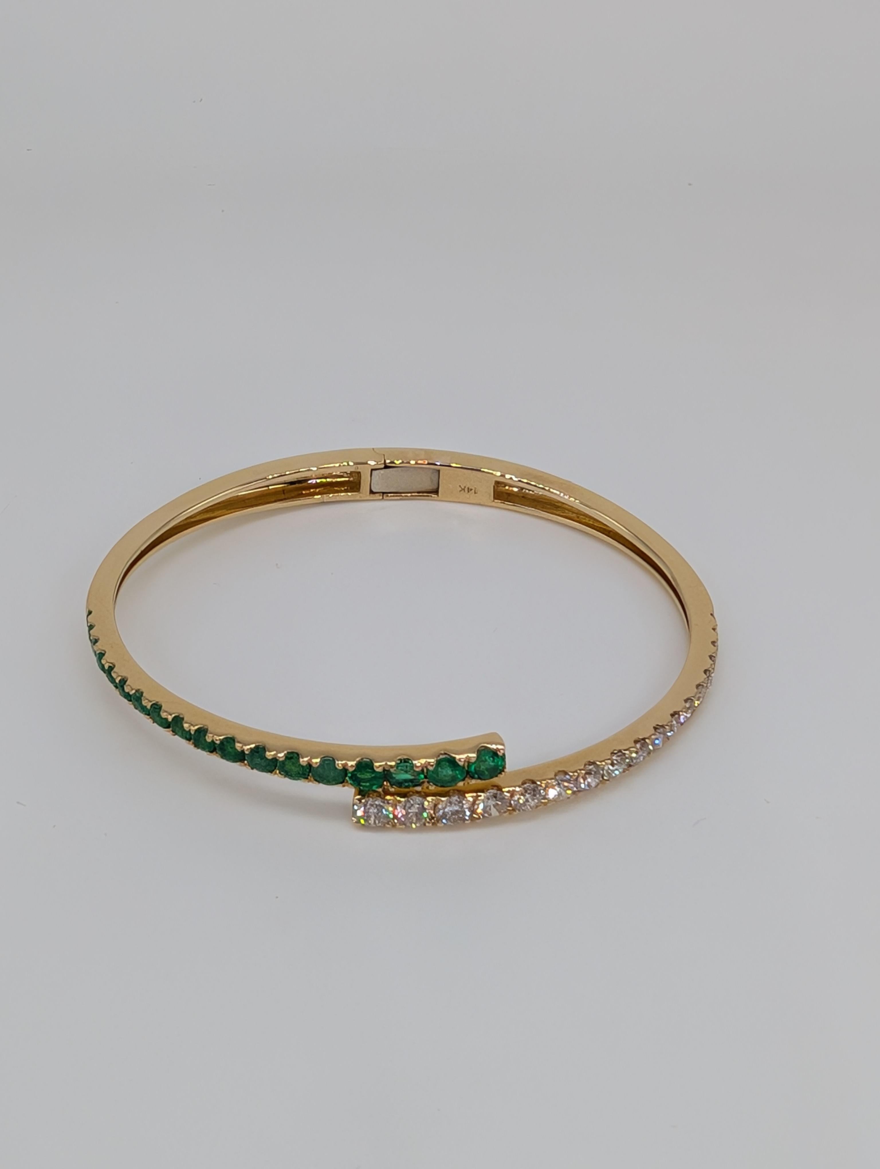 This 14-karat yellow gold bypass bangle is a stunning display of refined luxury and modern design. Featuring a graceful arrangement of graduated diamonds and emeralds, the piece showcases the diamonds (1.48ct) and emeralds (1.46ct) in an elegant,