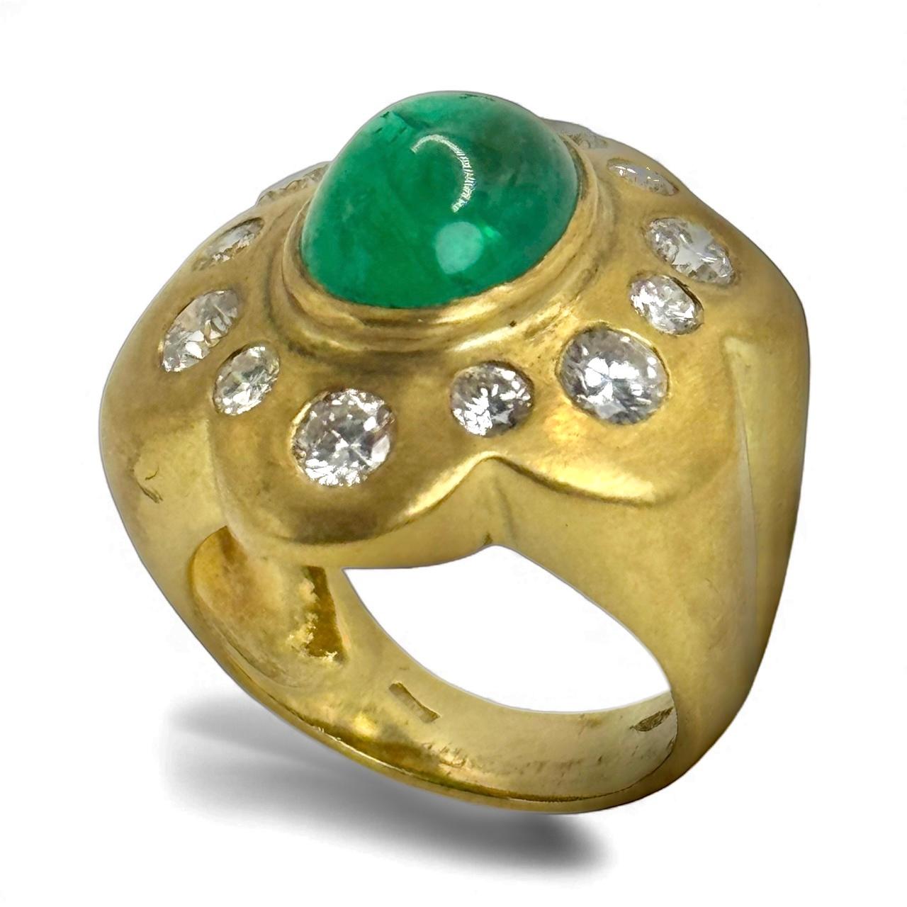 Cette bague vintage audacieuse en or jaune 14 carats est ornée d'une émeraude de taille cabochon aux teintes riches, entourée de douze diamants de taille brillant dans une monture sculpturale et légèrement bombée. Les contours organiques de la