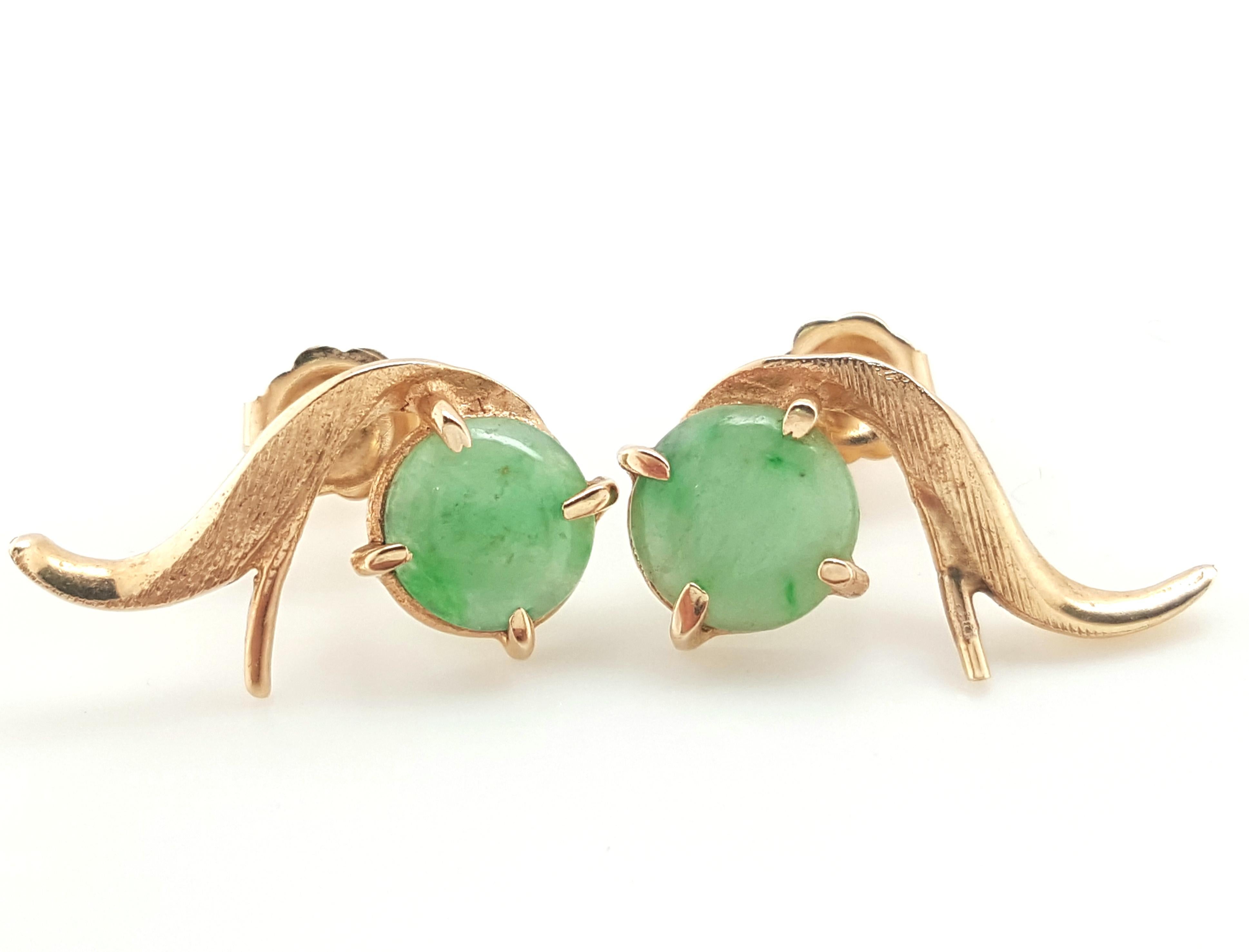 14 Karat Yellow Gold Cabochon Jadeite Jade Stud Earrings.  The earrings feature a pair of cabochon jadeite jade.  The jade are each set into a 14 karat yellow gold four prong setting, complemented by a sweeping ribbon of textured gold, completed by