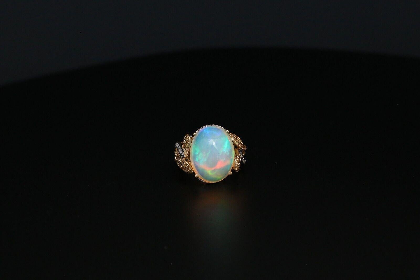 Cette exquise bague en or 14 carats ornée d'opales et de diamants est une pièce d'une élégance raffinée. La pièce maîtresse est une opale ovale fascinante, qui brille d'un jeu de couleurs éthéré, allant de l'orange ardent au bleu et au vert