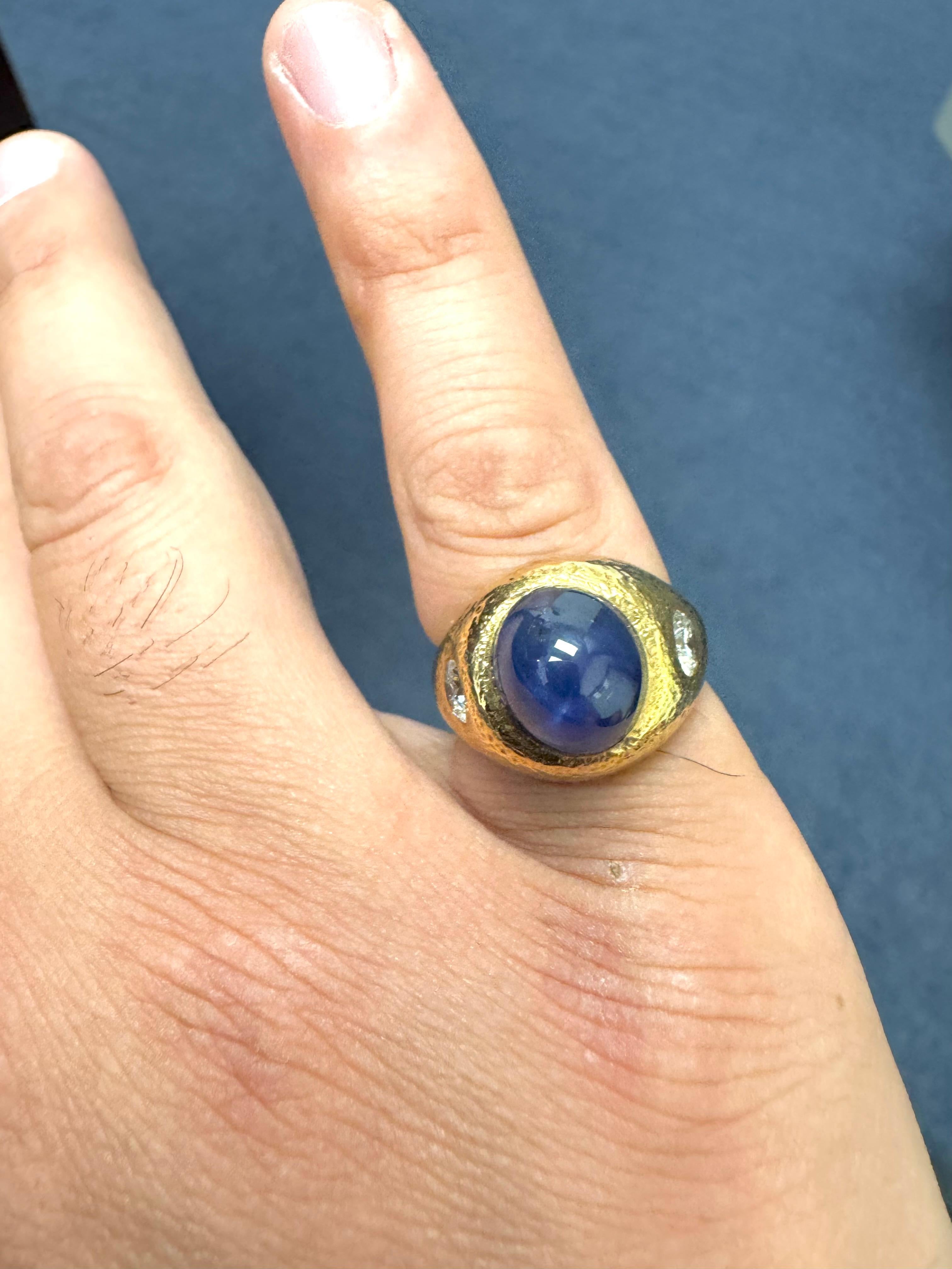 Un audaz y escultural anillo vintage elaborado en rico oro amarillo de 14 quilates, con un llamativo zafiro cabujón azul intenso como pieza central. El zafiro de cúpula alta está flanqueado por dos diamantes talla brillante, que añaden brillo y