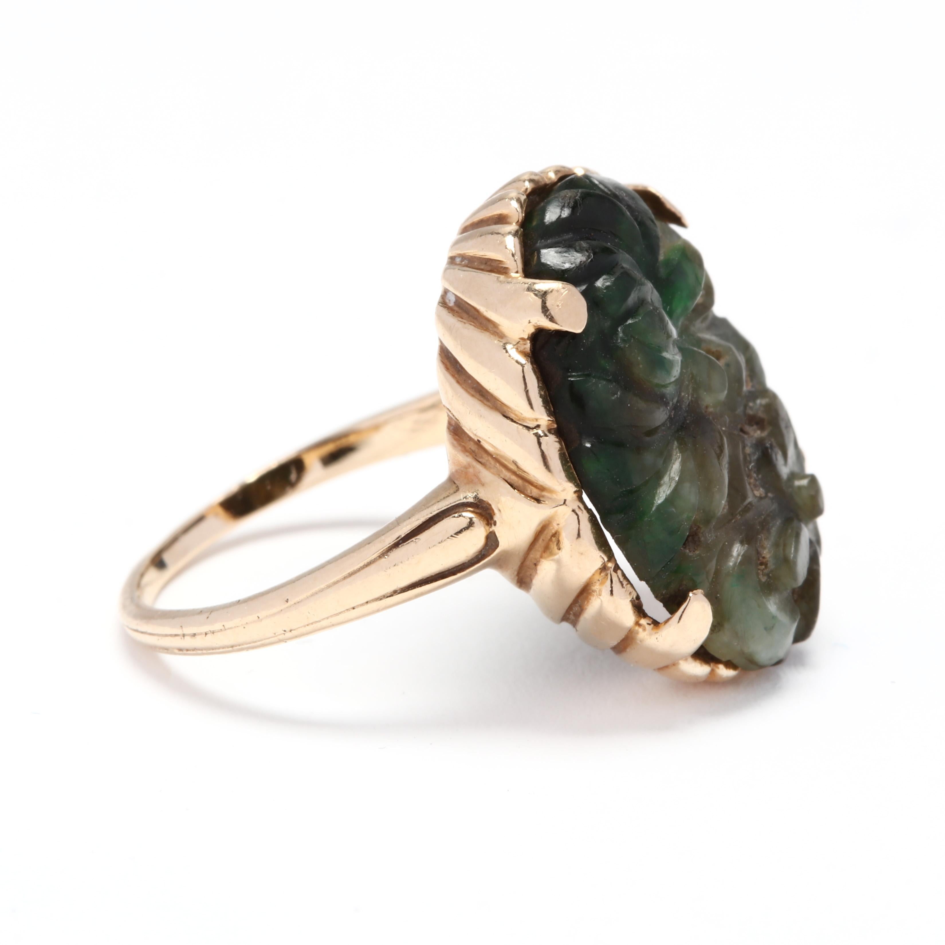 A 14 karat yellow gold and carved jade statement ring. This ring features a prong set, carved oval jade stone in a ridged mounting with a slightly tapered shank.

Stones:
- jade, 1 stone
- carved oval
- 18.75 x 14.6 mm

Length: 3/4 in.

Ring Size