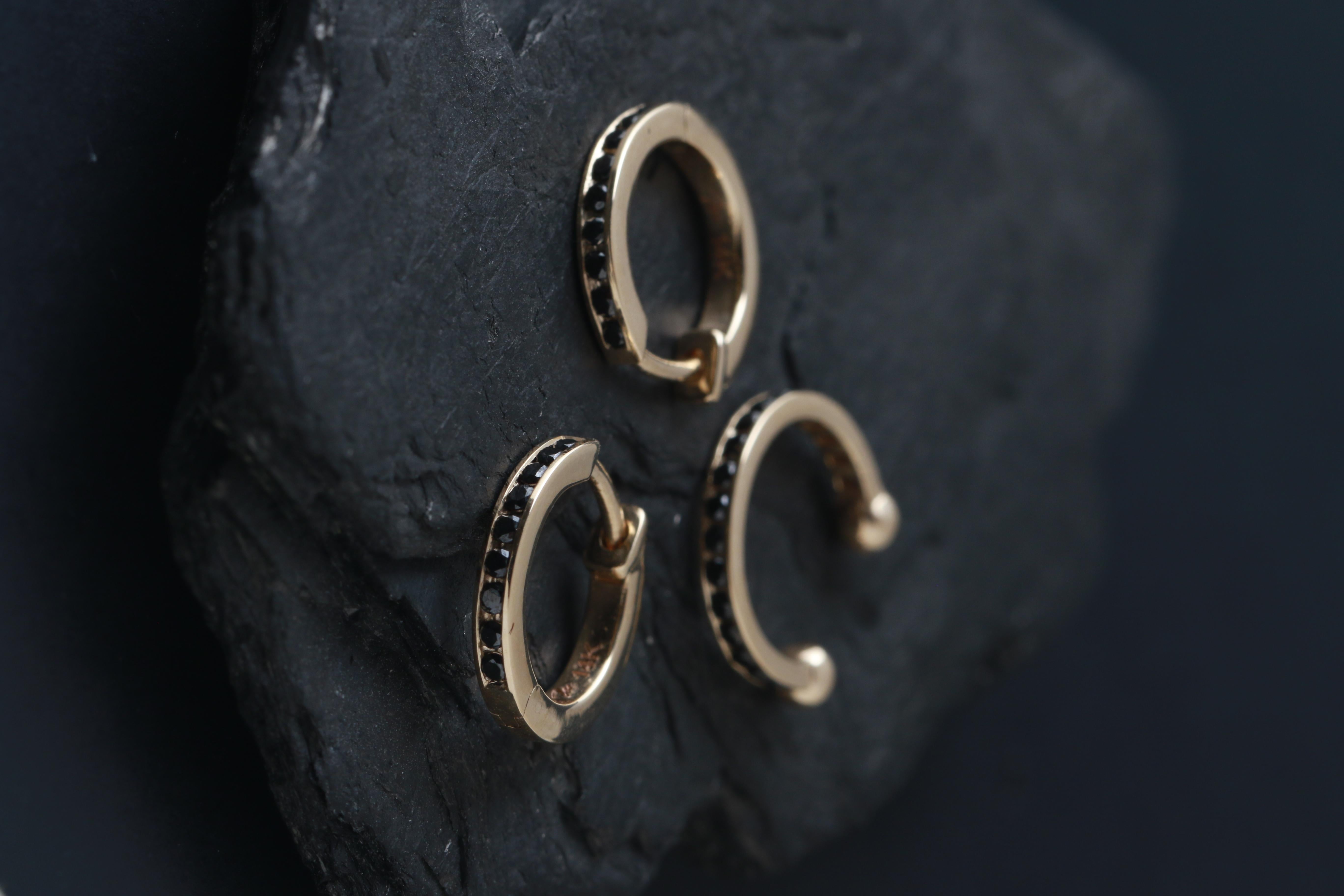 A row of black diamonds is channel set into a hinged hoop style. 

Full cut round black diamonds, 1.2mm each, total carat weight of 0.11 carats.
14k Yellow gold

