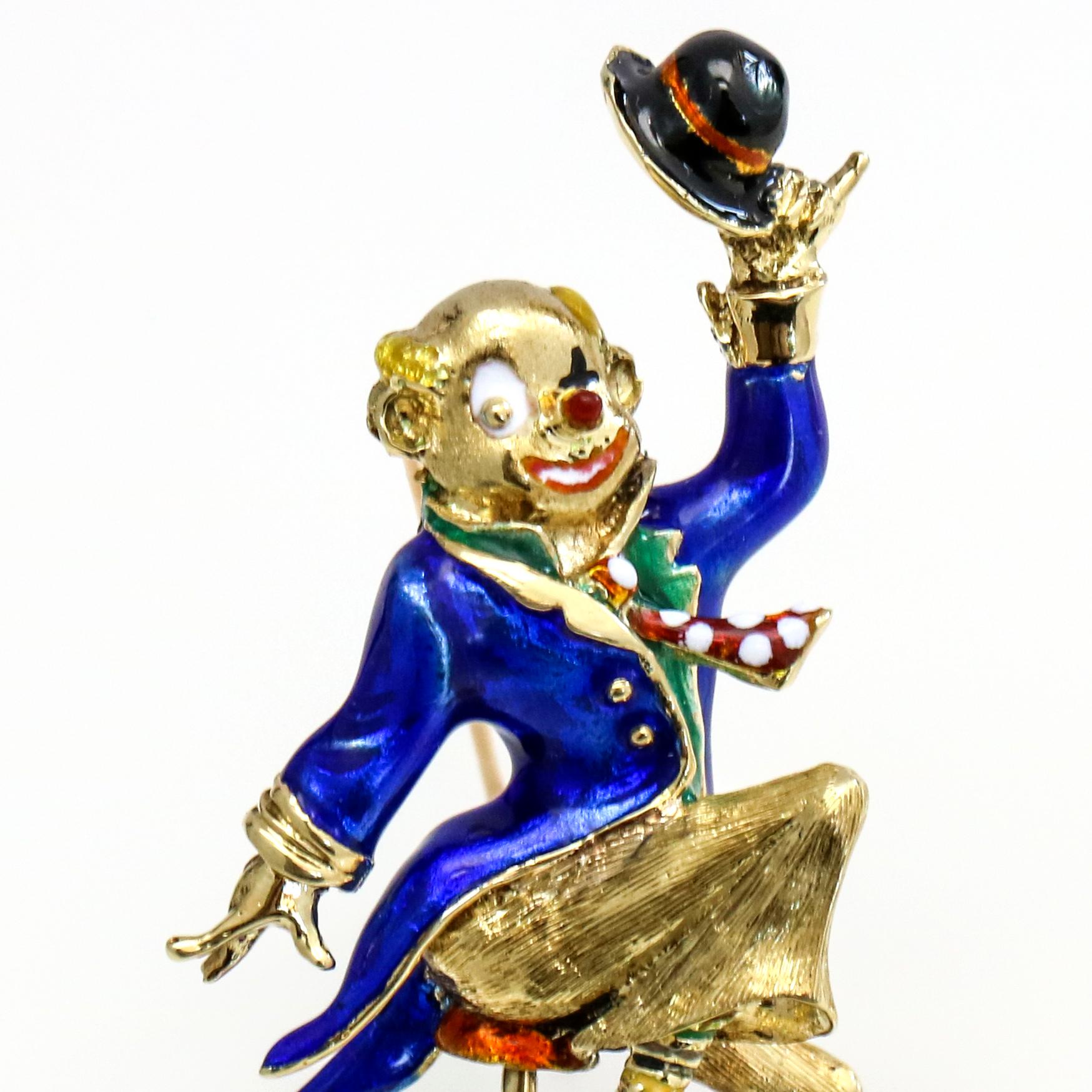 A clown riding a unicycle holding a hat brooch with enamel paint and textured metal details in 14-karat yellow gold. The wheel spins.