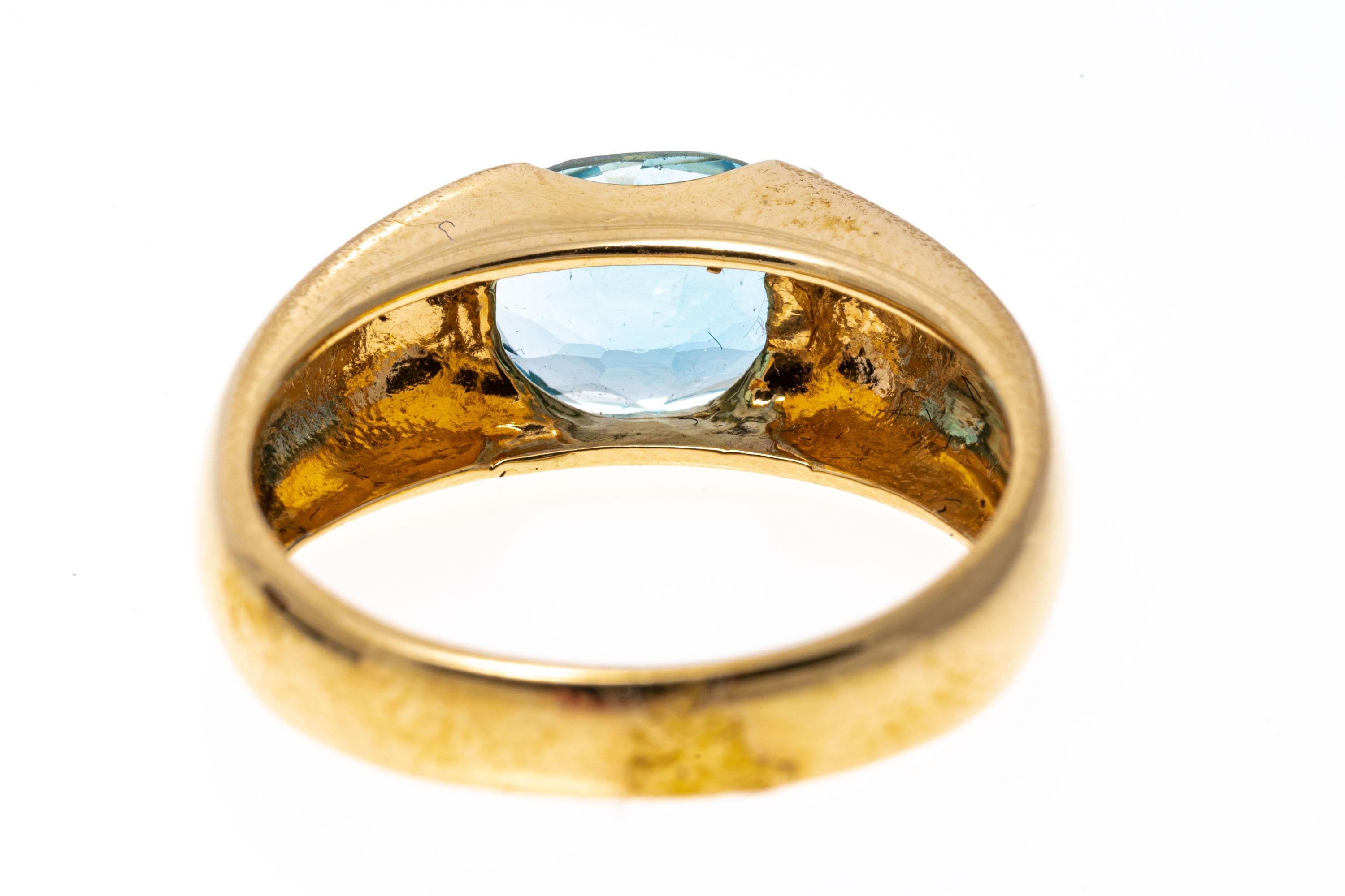 14k yellow gold ring. This handsome, contemporary ring is a horizontal, oval faceted, medium blue color blue topaz, approximately 1.97 CTS, half flush set into wide, high polished gold shoulders.
Marks: 14k
Dimensions: 5/16