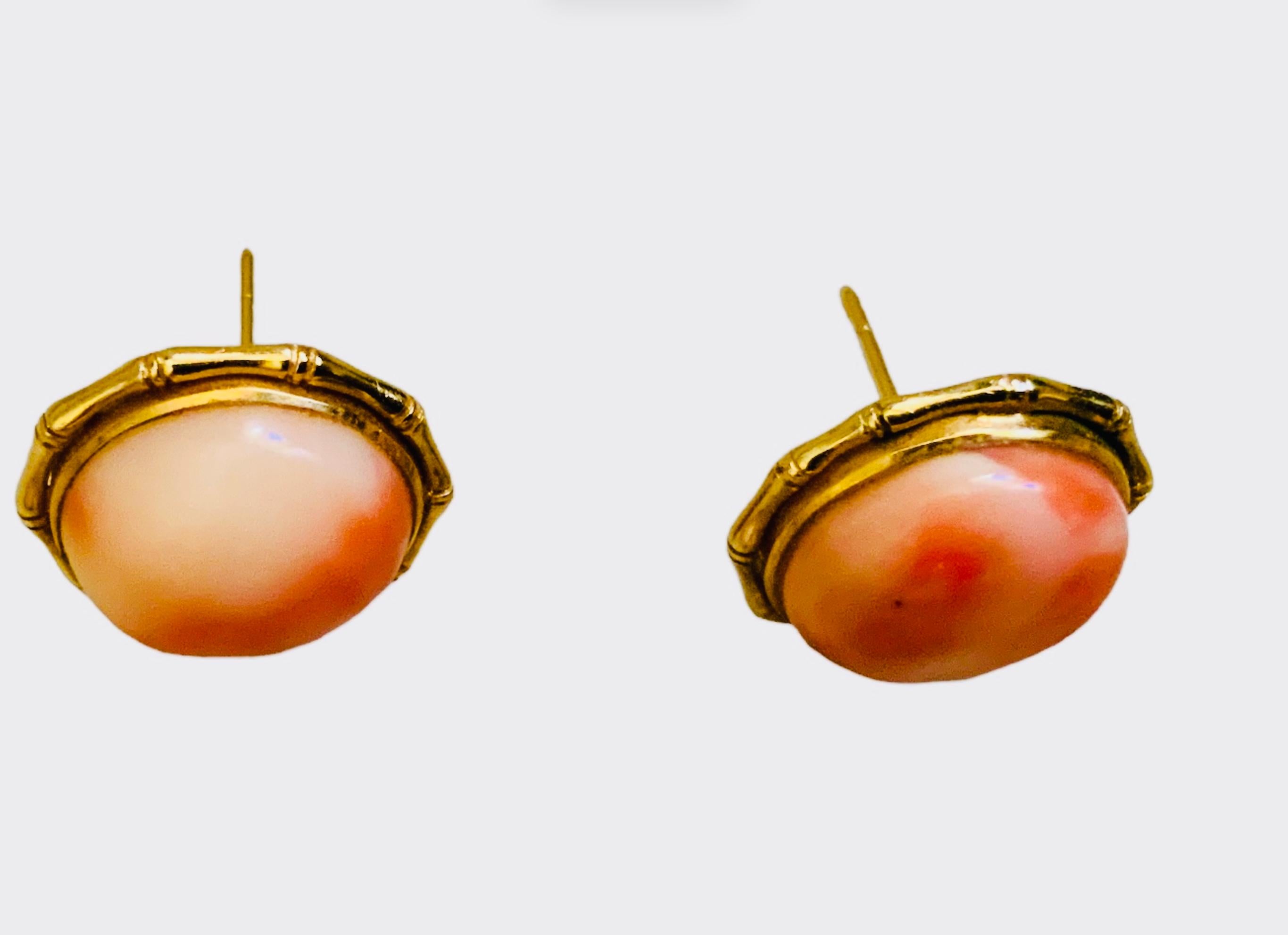 This is a 14K Gold Coral Pair of Earrings. It depicts a pair of round cabochon Corals mounted in 14 K yellow gold frames shaped as bamboo sticks joined together.