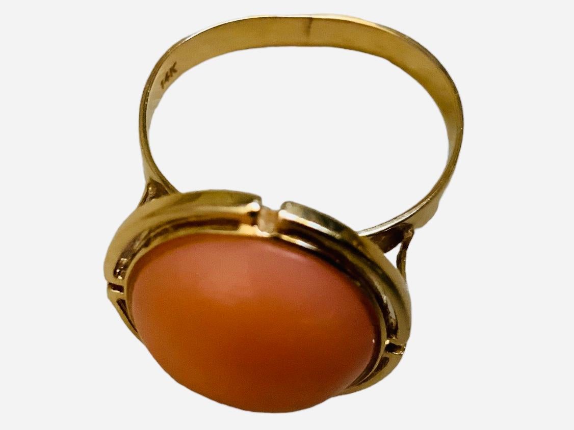 Dies ist 14K Gelbgold und Korallen Ring. Er zeigt einen ovalen Korallen-Cabochon in einem ovalen, in vier Bögen geschliffenen Halo aus 14 Karat Gold. Er ist auf der Rückseite des Schafts mit 14k gestempelt.