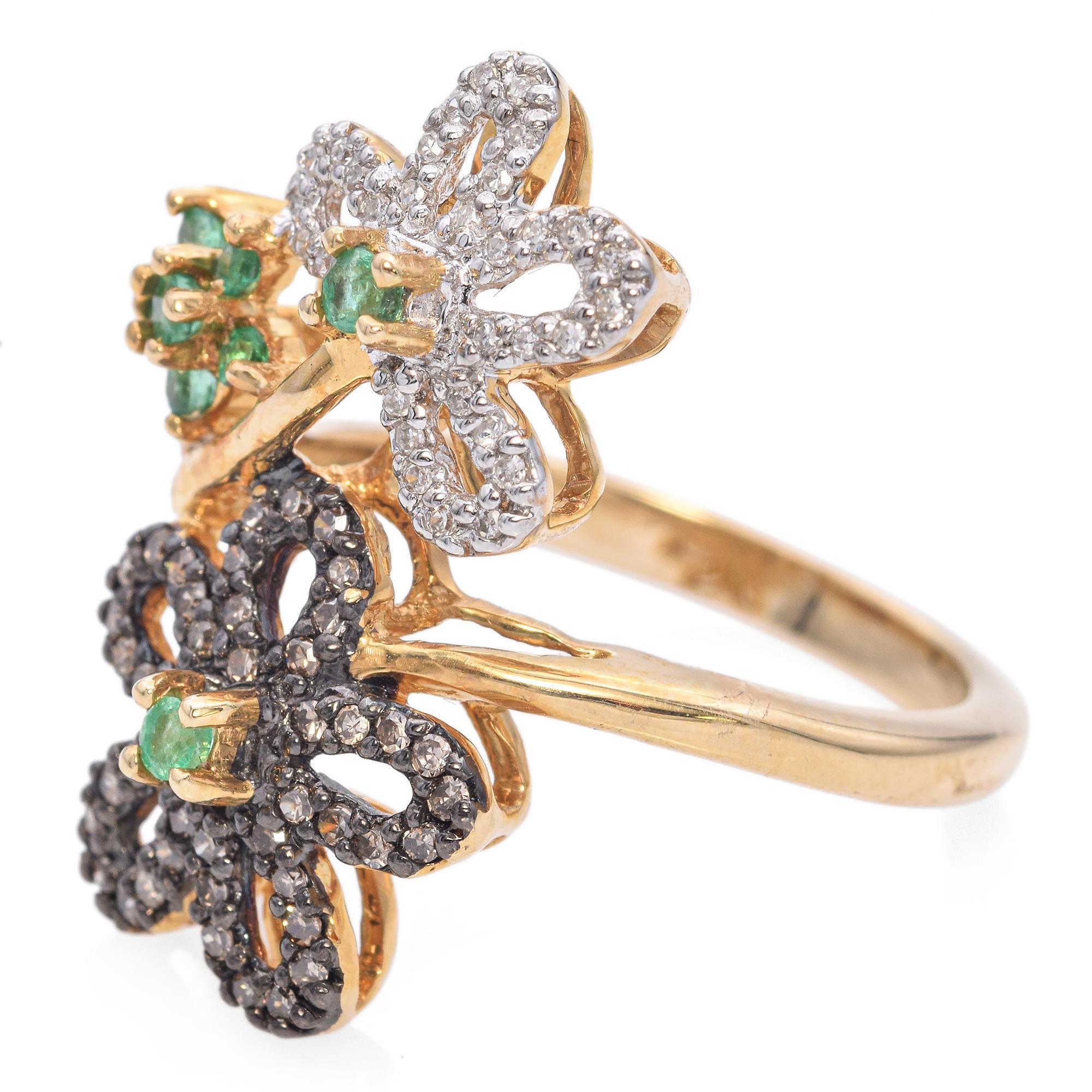 A striking ring featuring three floral motifs adorned with sparkling stones.
The flowers are embellished with white and champagne diamonds, accented by vibrant green emerald centers, creating a captivating contrast.
They are set in a warm gold band,