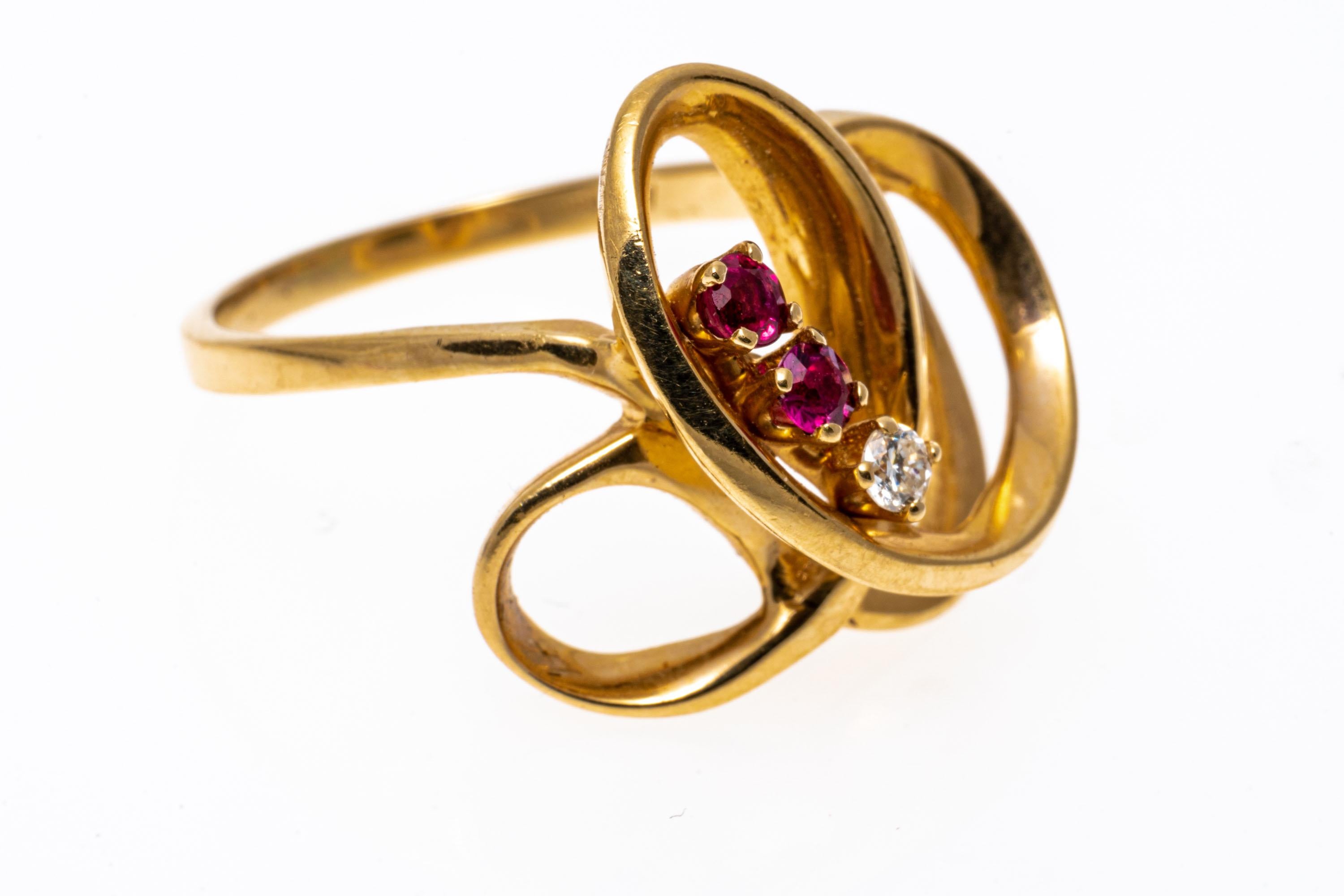 14k yellow gold ring. This contemporary ring is a high polished, yellow gold open swirl style, decorated with two round faceted, pinkish red rubies, approximately 0.18 TCW, and one round faceted diamond, 0.04 CTS, prong set.
Marks: None, tests