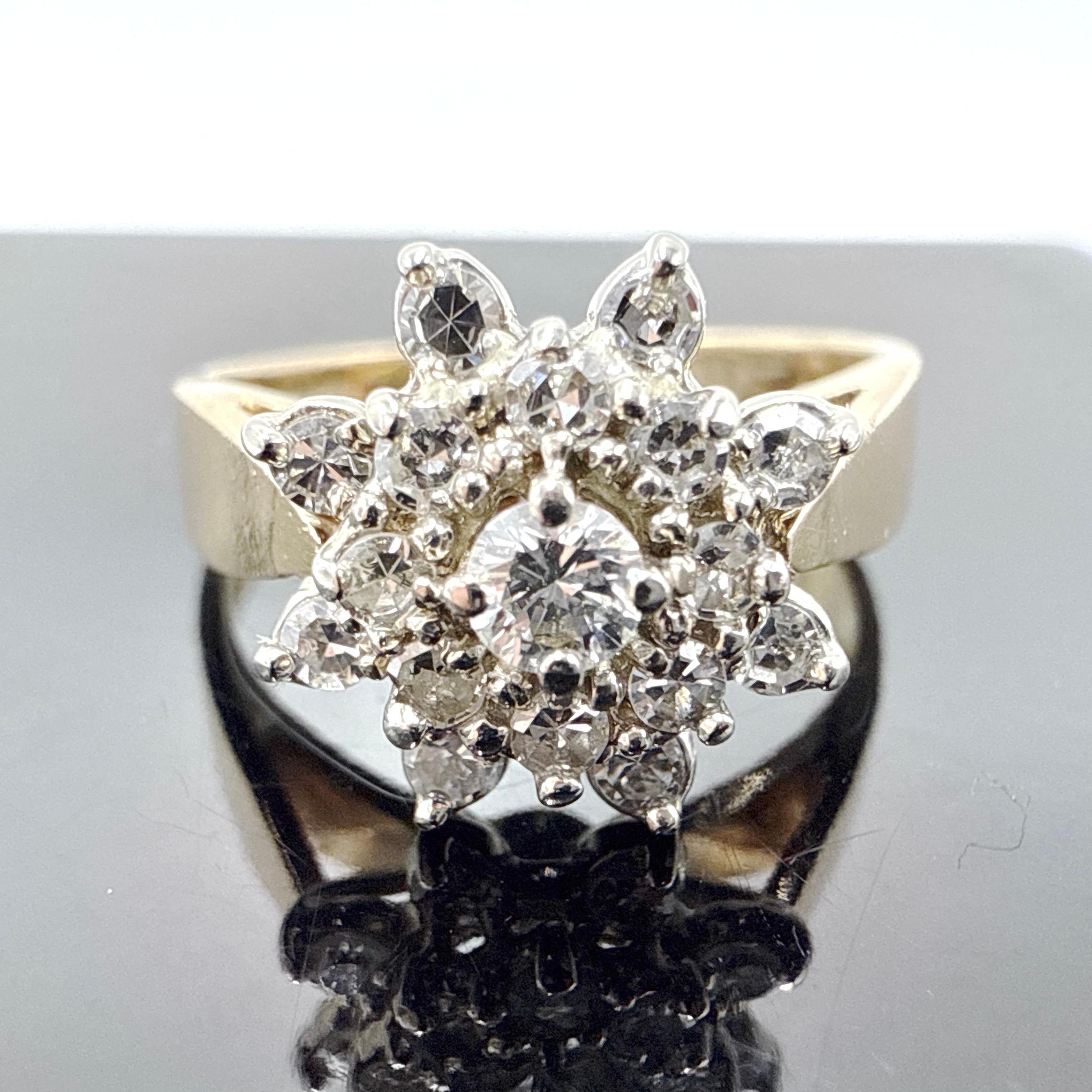This 14K yellow gold engagement ring features a classic diamond cluster design, crafted through wax casting and hand finishing. It offers a symmetrical and structured aesthetic with a raised central setting and two-tiered diamond accents.

Design