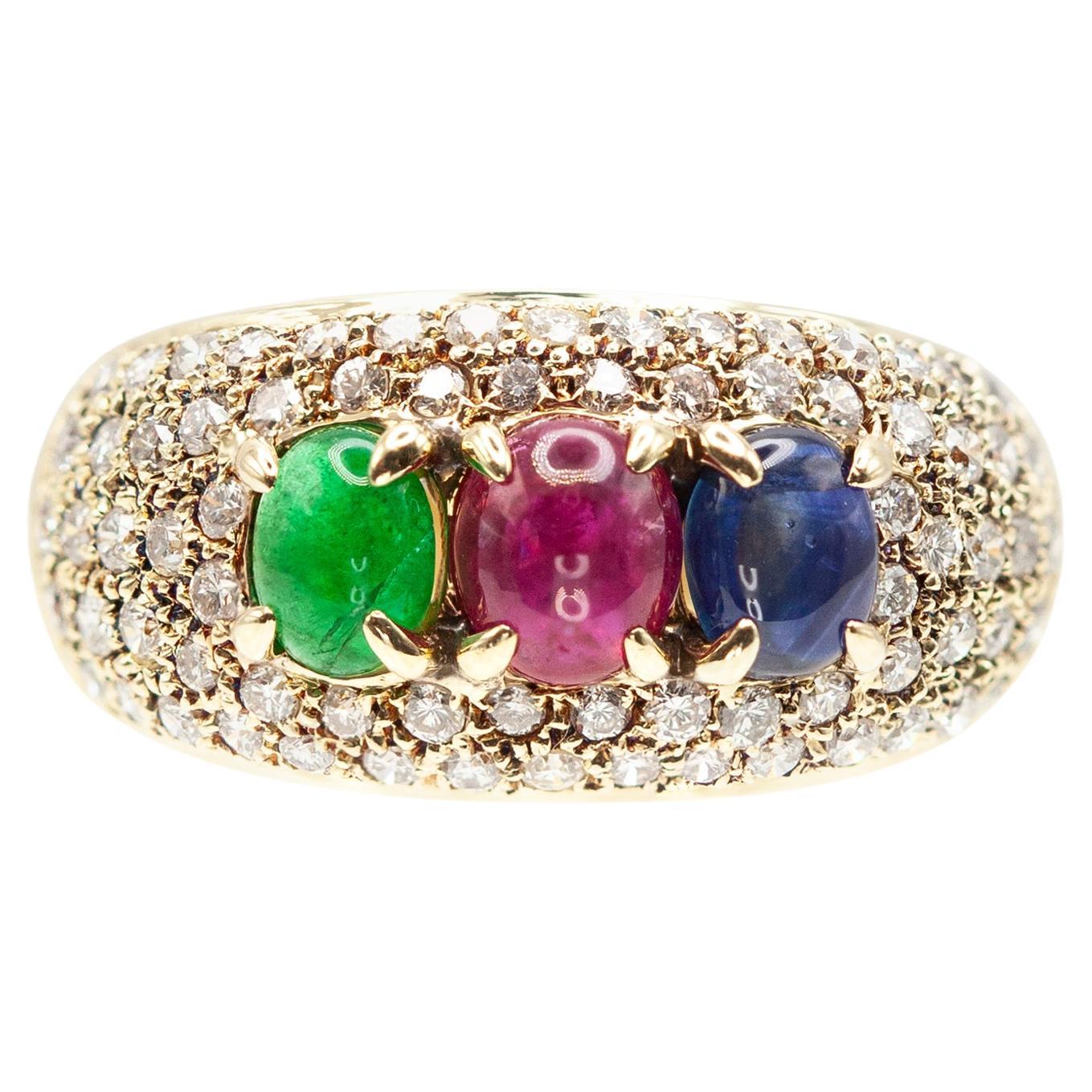 This striking band features a trio of oval cabochon gemstones — a vivid green emerald, a rich red ruby, and a deep blue sapphire — each set in secure prongs. The gemstones are framed and flanked by a glittering field of brilliant-cut diamonds in a