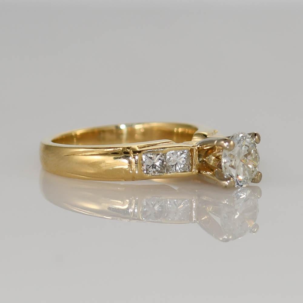 Diamond engagement ring in 14k yellow gold.
Tests 14k and weighs 4.8 grams.
The center diamond is a round-transition cut, .75 carats, G to H color, VS clarity.
The side diamonds are princess cuts, .32 total carats, H color, VS clarity.
Ring size is