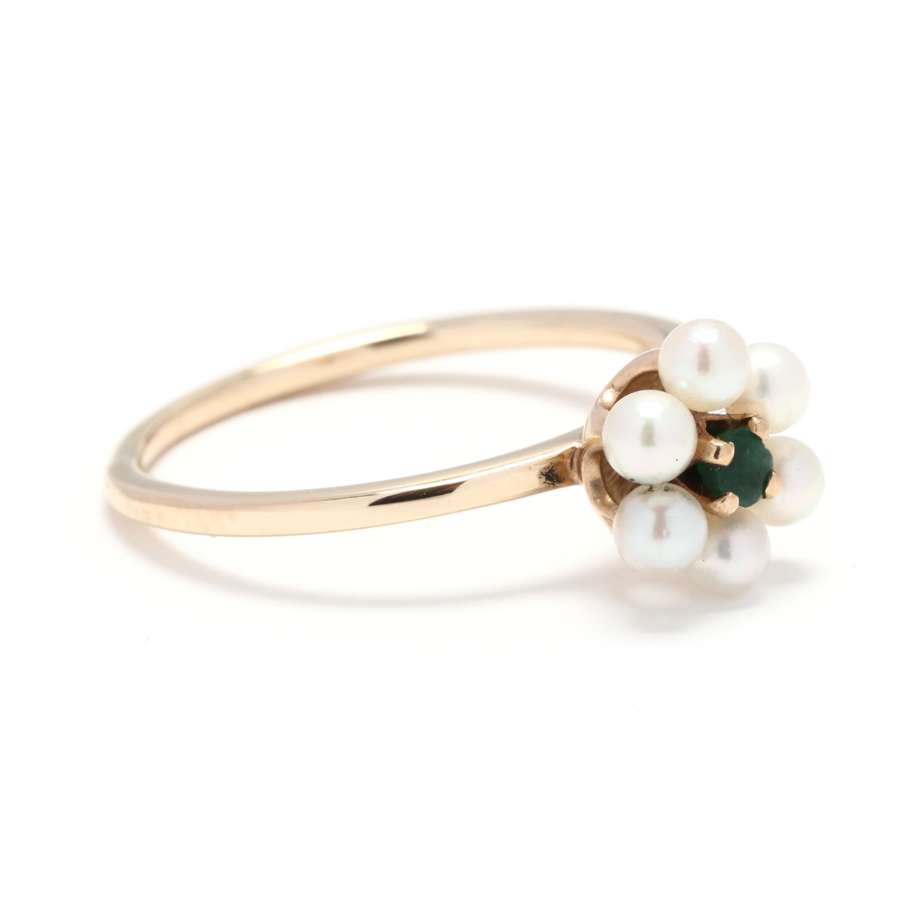 A 14 karat yellow gold, emerald and pearl flower ring. This ring is centered on a round cut emerald surrounded by a pearl halo to create a floral motif and set atop a thin band.

Stones:
- emerald, 1 stone
- round cut
- 2.75 mm

- pearls, 6 stones
-