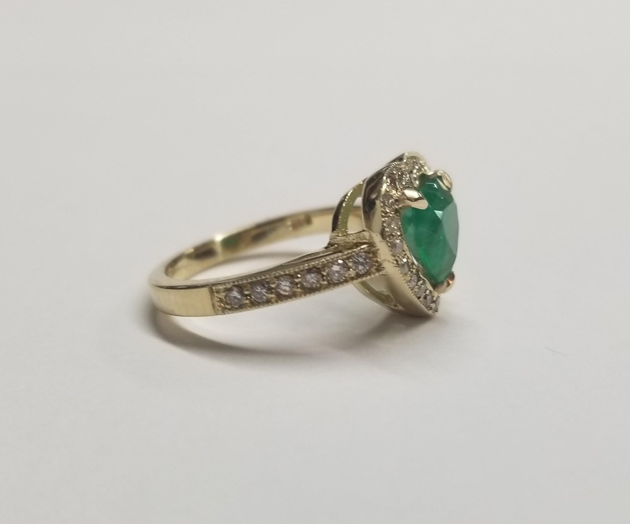 Anello in oro giallo 14k con smeraldo a forma di cuore e diamanti, contenente uno smeraldo a forma di cuore di qualità gemmologica del peso di 1,32 carati e 32 diamanti rotondi a taglio pieno di qualità finissima del peso di 0,45 carati.  Questo
