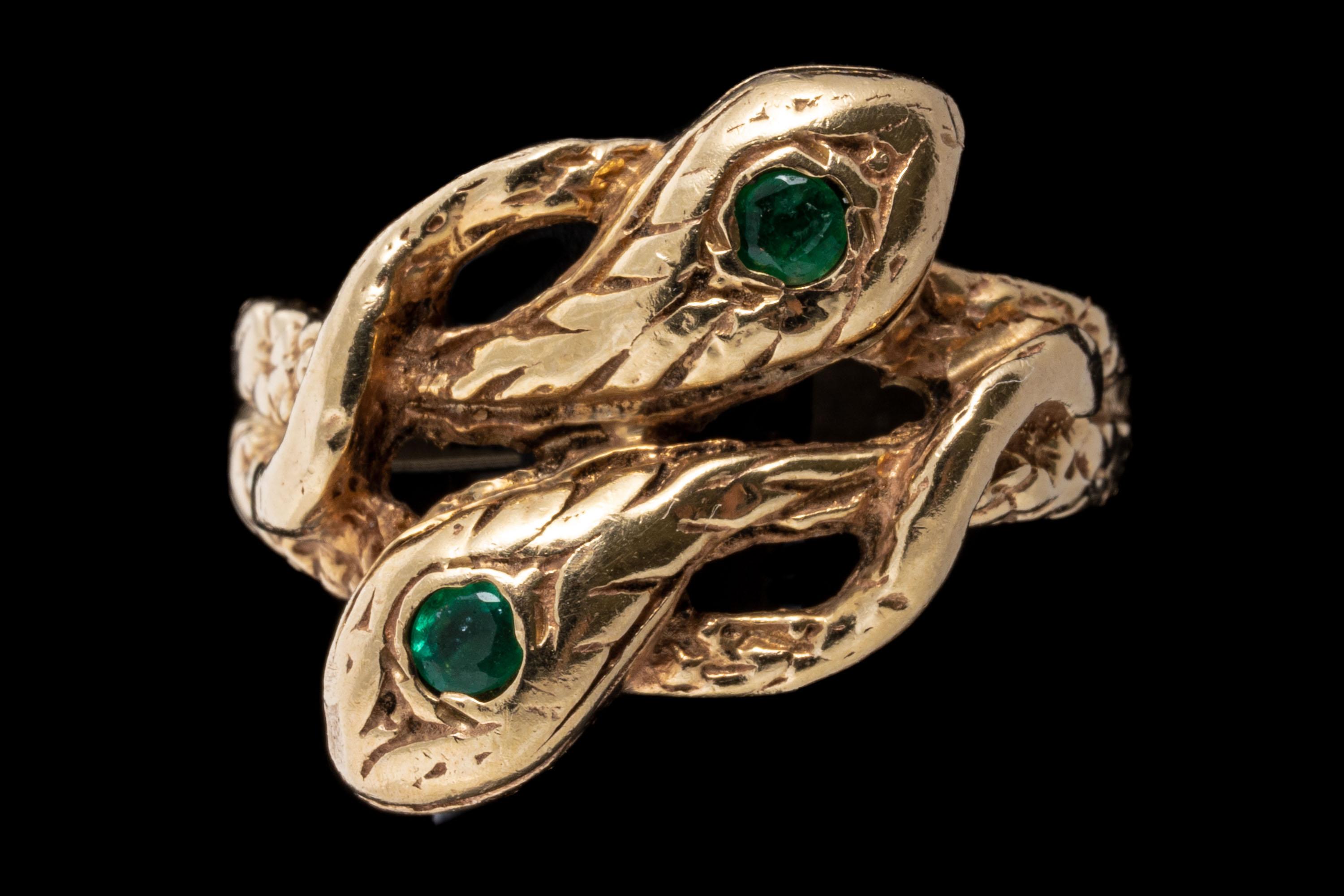 14k yellow gold ring. This beautiful ring is an intertwining serpent motif of two bypassing snakes, with a patterned finished body, finished by two round faceted, green emeralds, approximately 0.14 TCW decorating each of the heads, flush set.
Marks: