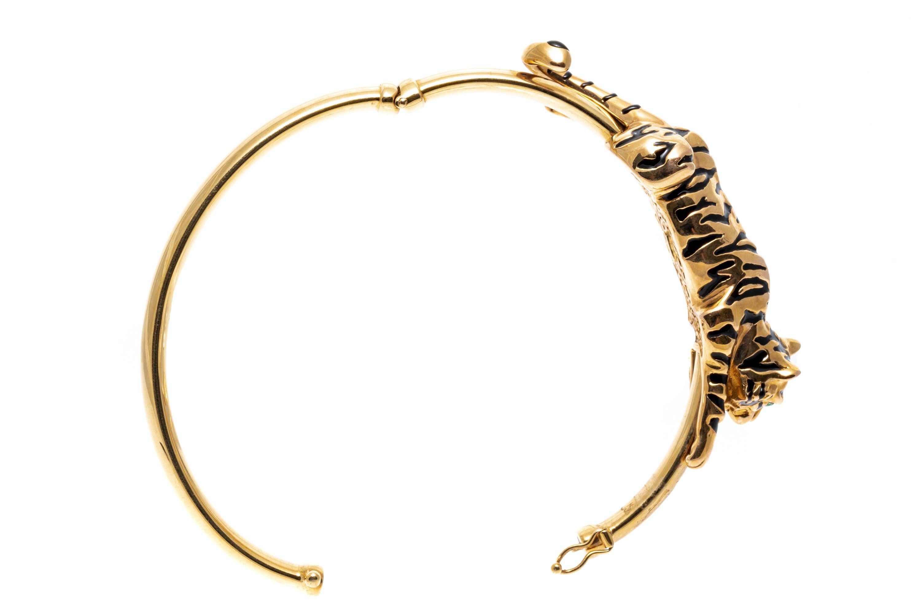 Armband aus 14k Gelbgold. Dieser fabelhafte Armreif mit Scharnier zeigt einen schönen, figuralen, galvanisch geformten Tiger, der mit schwarzen Emaille-Streifen und runden, facettierten Smaragdaugen verziert ist (ca. 0,06 TCW). Das Armband verfügt