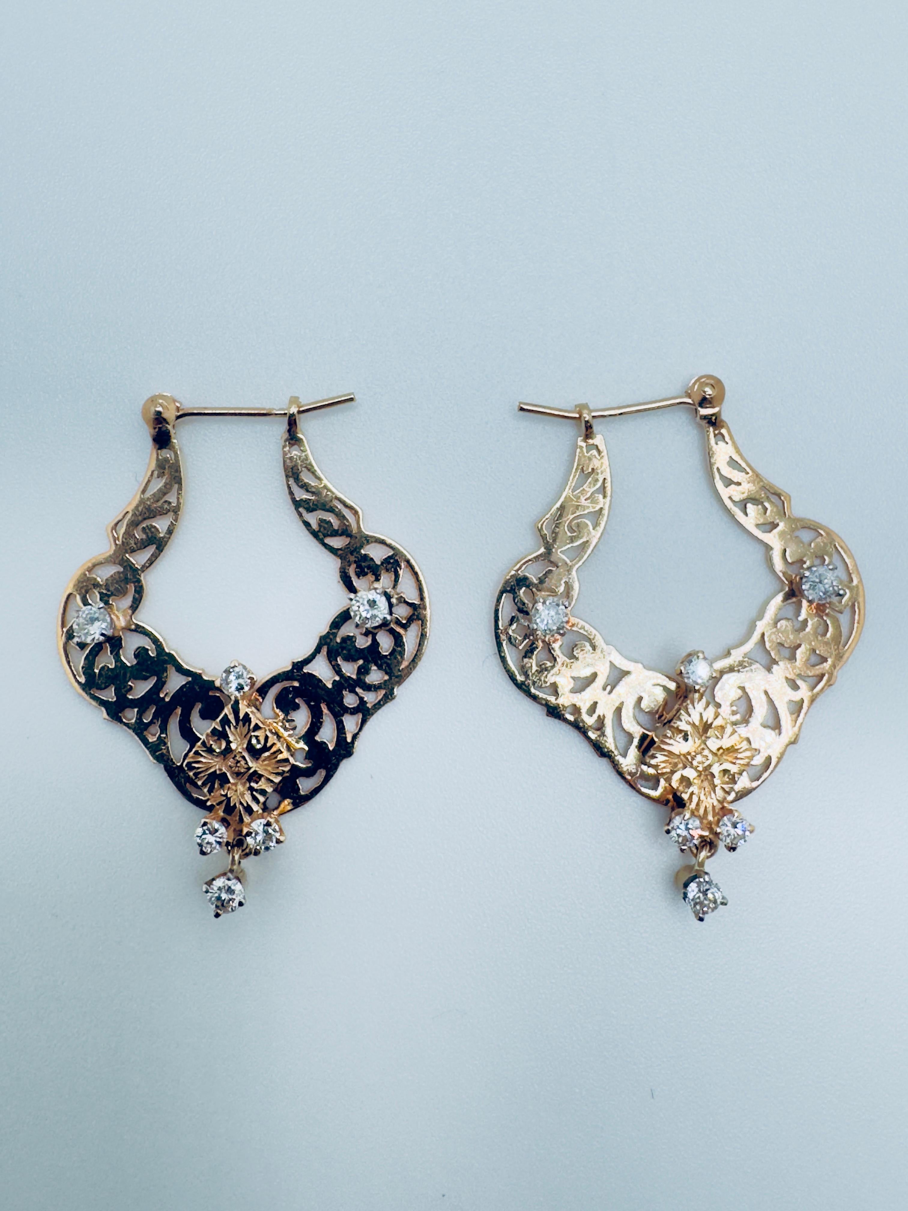 Ces exquises boucles d'oreilles demi-boucles en or jaune 14 carats présentent un délicat travail de filigrane avec des motifs tourbillonnants et floraux, reflétant un savoir-faire artisanal complexe et une élégance intemporelle. Chaque boucle