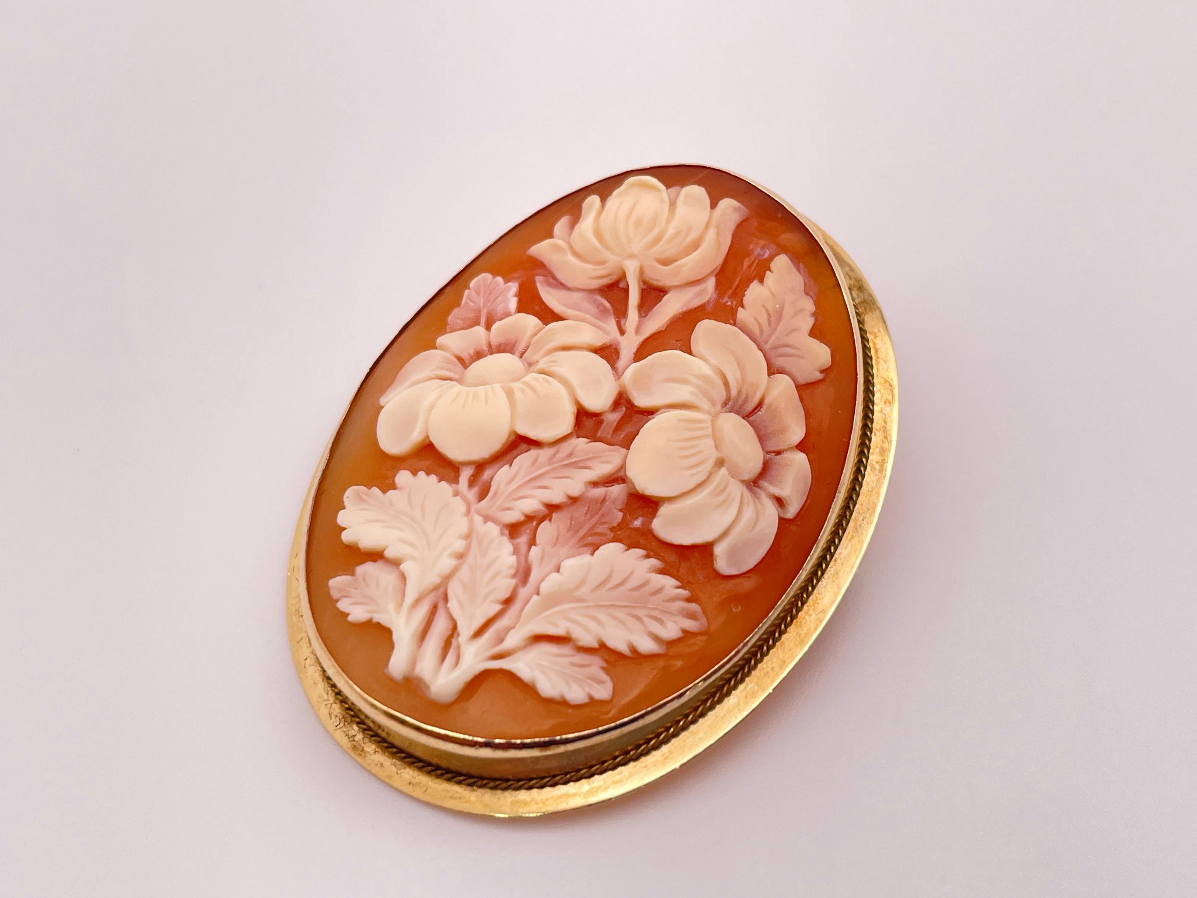 An original vintage hand carved floral shell cameo set in a 14K yellow gold frame.

This beautiful cameo depicts a delicate bouquet of flowers, each with finely etched petals and leaves emerging from the natural layers of the shell in graceful