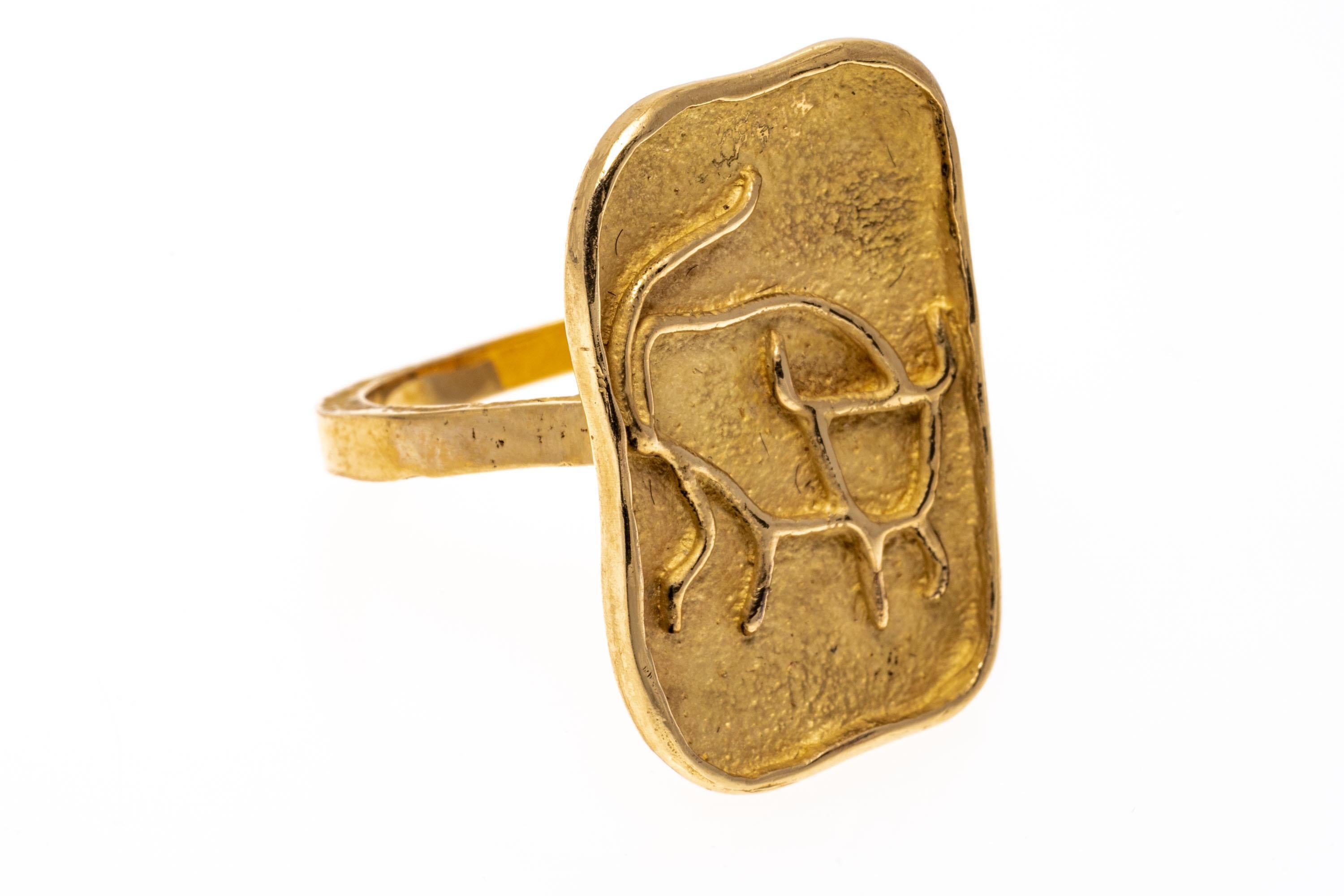 14k yellow gold ring. This striking yellow gold ring has a free-form rectangular center, decorated with a high polished relief of a line drawn Taurus bull motif, edged with a raw-edged shank.
Marks: 14k
Dimensions: 9/16