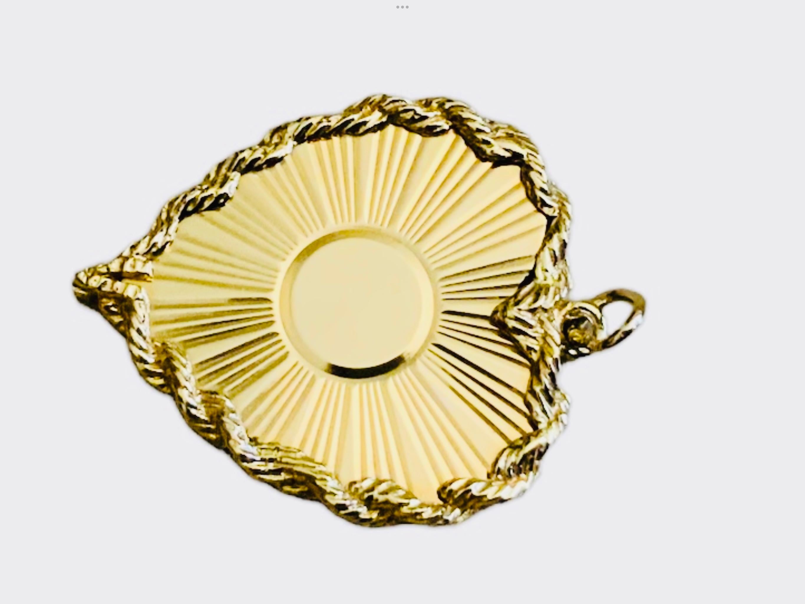 This is an 14K yellow gold heart pendant. It depicts a heart with a circular center and some sun rays (reeded metal) coming out from it. The whole border of the heart is adorned with a rope chain. An oval gold ring is attached to the pendant to be