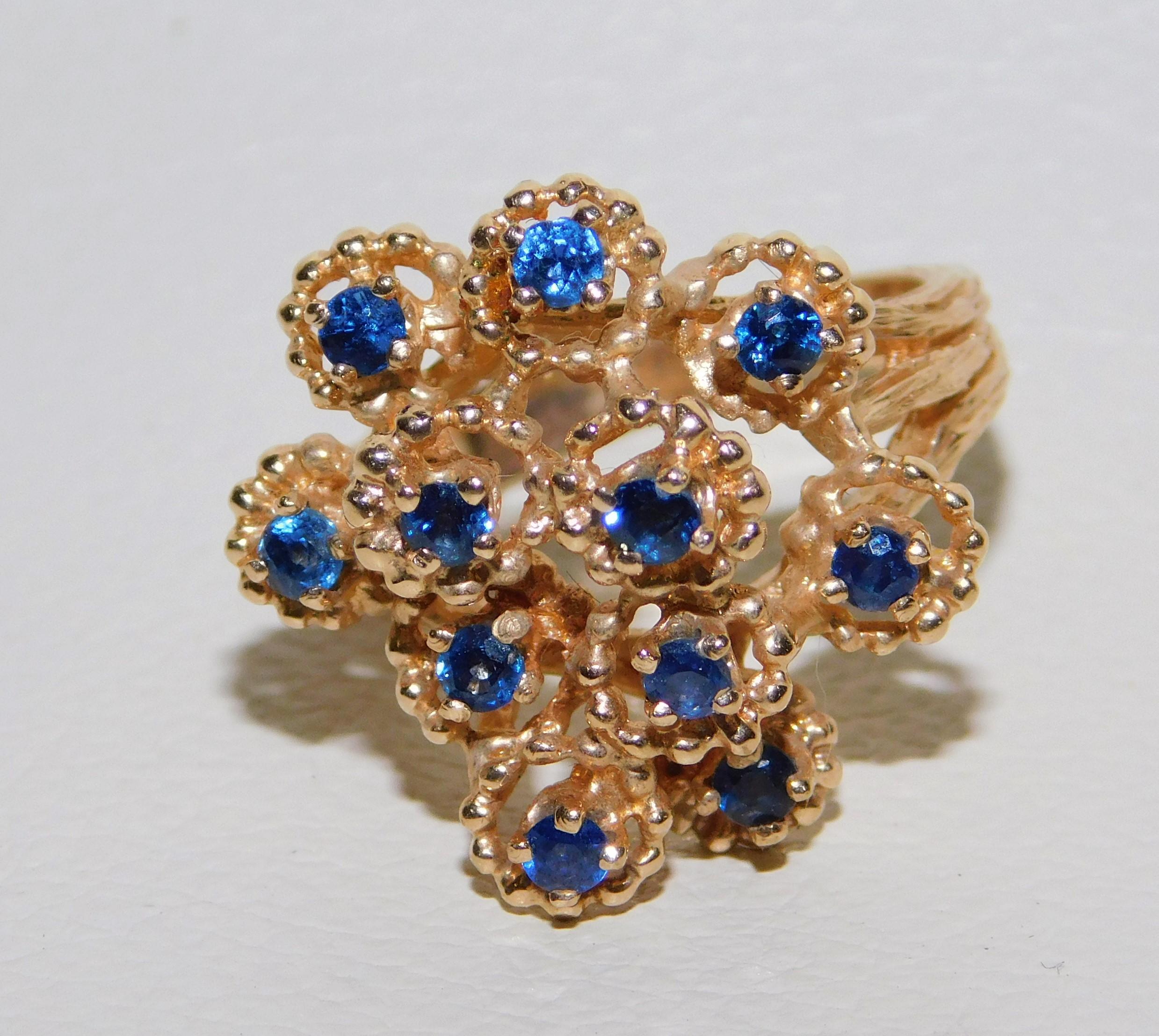 Stamped 14-karat yellow gold ladies gemstone ring with a bright polish and textured finish. Condition is very good. Ladies cocktail ring with blue sapphire gemstones in a floral design. Each gem is surrounded by a textured gold detail. Shank