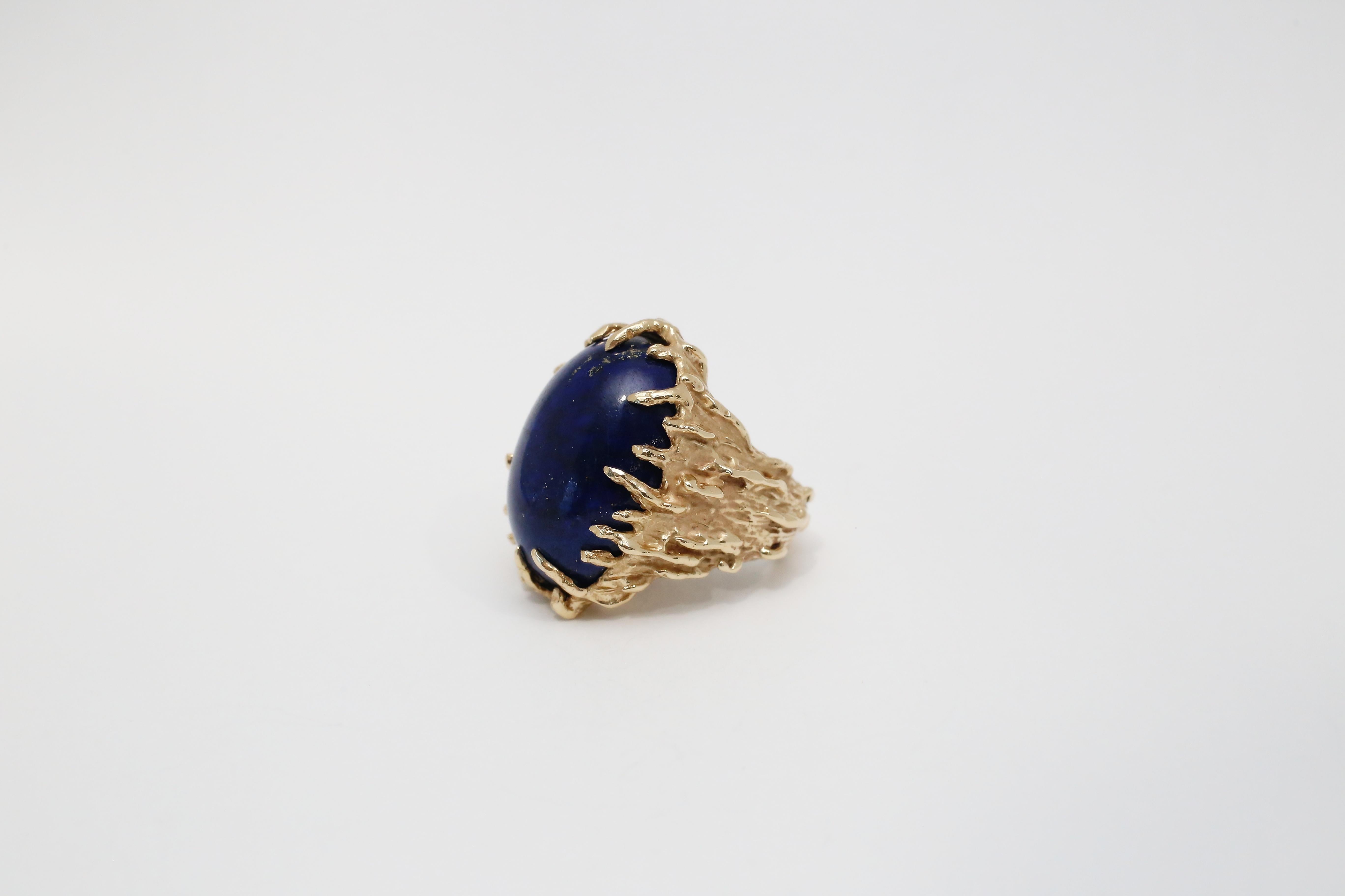 This bold and striking 14k yellow gold ring features a large, oval cabochon-cut lapis lazuli gemstone in a rich, royal blue hue. The deep blue stone is set in a dramatic, organic-style claw prong setting, surrounded by textured gold detailing that