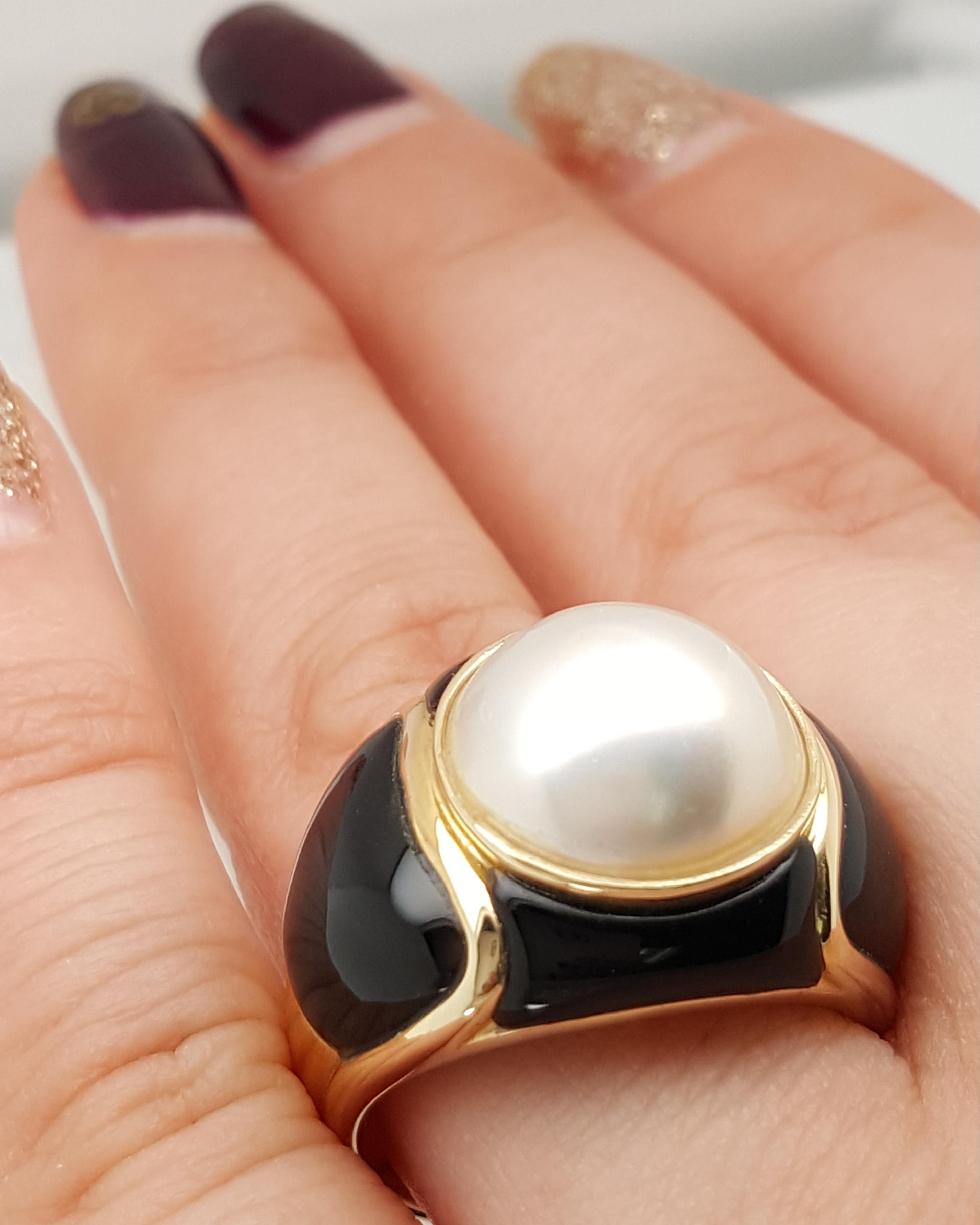 14 Karat Yellow Gold Mabe Pearl and Black Onyx Ring. This bold ring features a Mabe pearl surrounded by four pieces of carved black Onyx beautifully inlaid on the shoulders of the ring.  The ring weighs 8.71 grams. Shank tapers from 16.63 - 3.91 