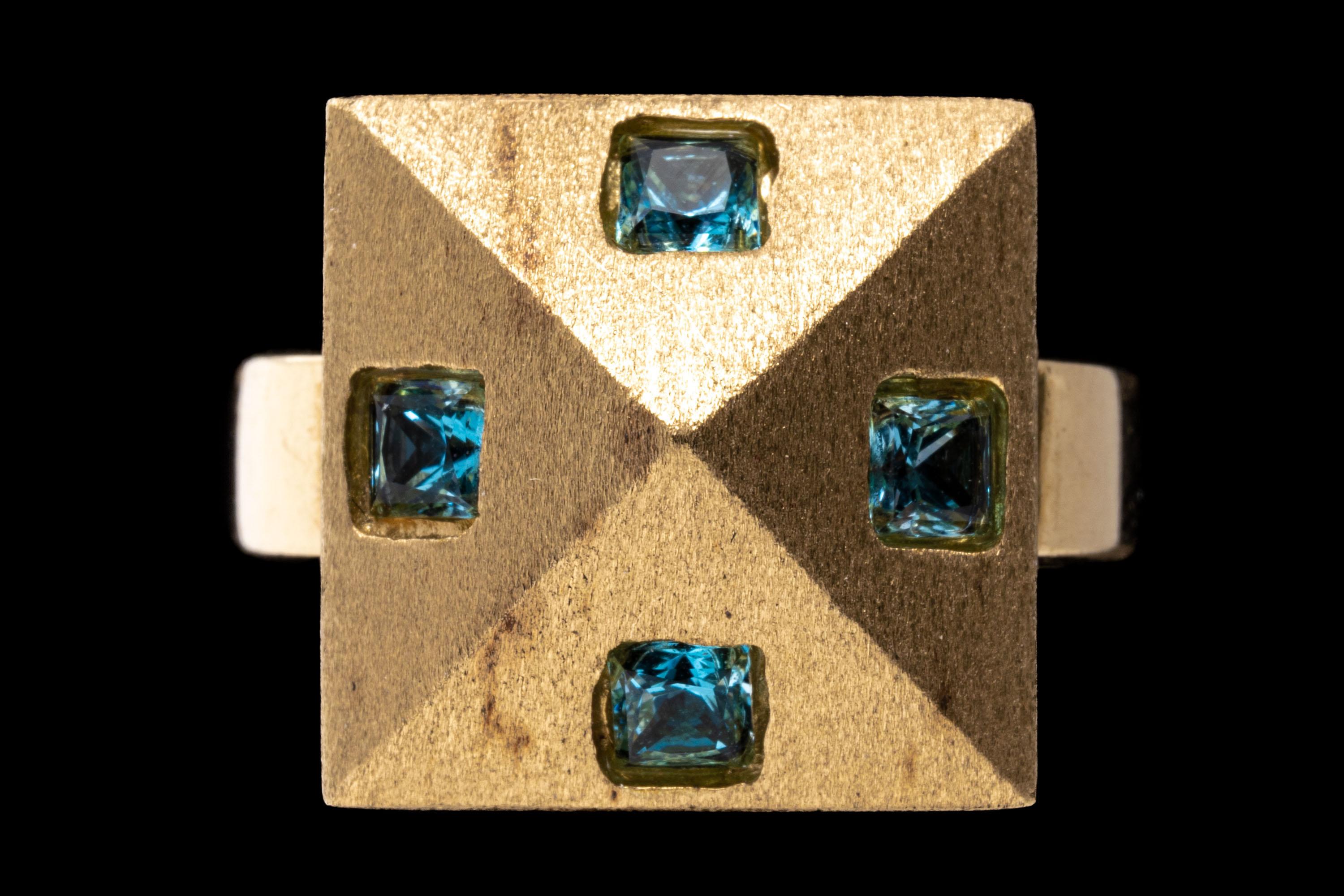 14k yellow gold ring. This unique ring has a square, shallow domed pyramid shaped top, sandblasted finished and flush set with four, square faceted, pale blue color blue topaz, flush set, approximately 0.32 TCW and finished with a wide, high