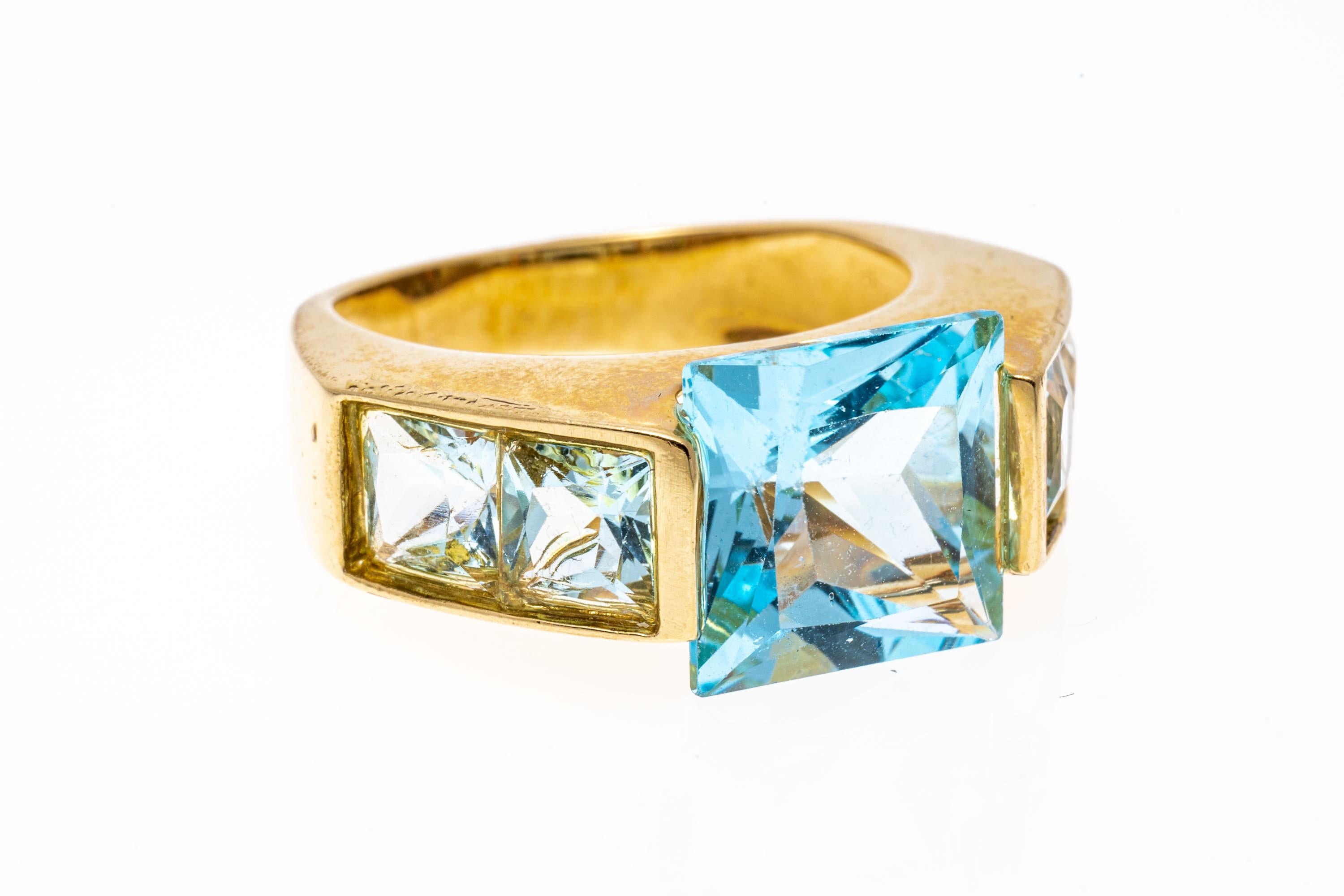 14k yellow gold ring. This modern ring has a square faceted, light blue color blue topaz center, approximately 5.00 CTS, set with a wide half bezel and decorated with angled shoulders, set with square faceted, pale blue color blue topaz, channel