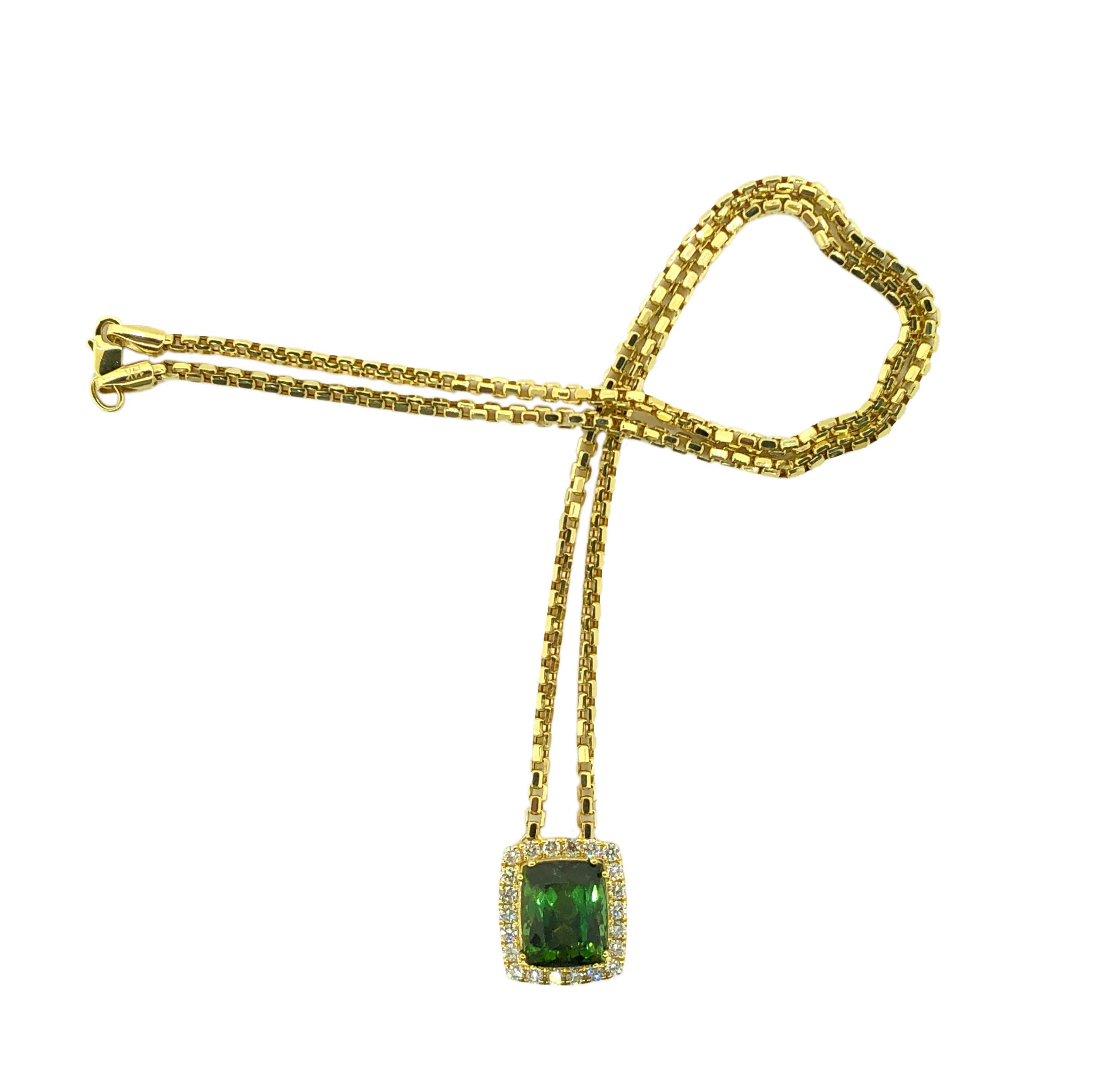 Showcasing a stunning and vibrant Green Tourmaline Necklace. The pendant offers a perfectly set center Cushion Cut Tourmaline, surrounded by two rows of round brilliant cut Round Diamonds suspended from a beautiful 22 inch chain, all in Yellow Gold.