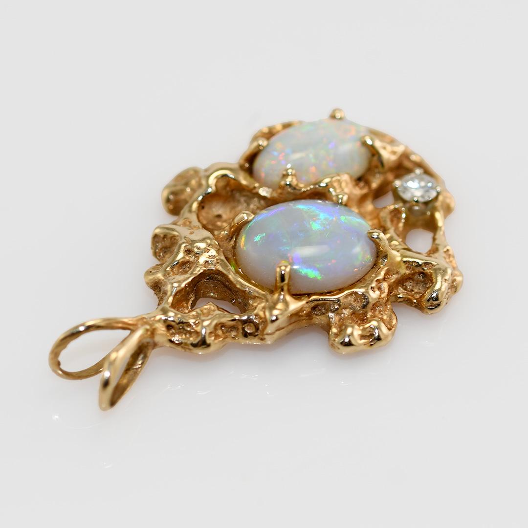 Opal- und Diamant-Anhänger in einer Nugget-Fassung aus Gelbgold.

Der Anhänger besteht zu 54% aus Gold und wiegt 13,5 Gramm brutto.

Die Opale messen 11 x 9,5 mm und 10,8 x 6,4 mm.

Blaue, grüne und rote Farben.

Es ist ein .12 Karat runder