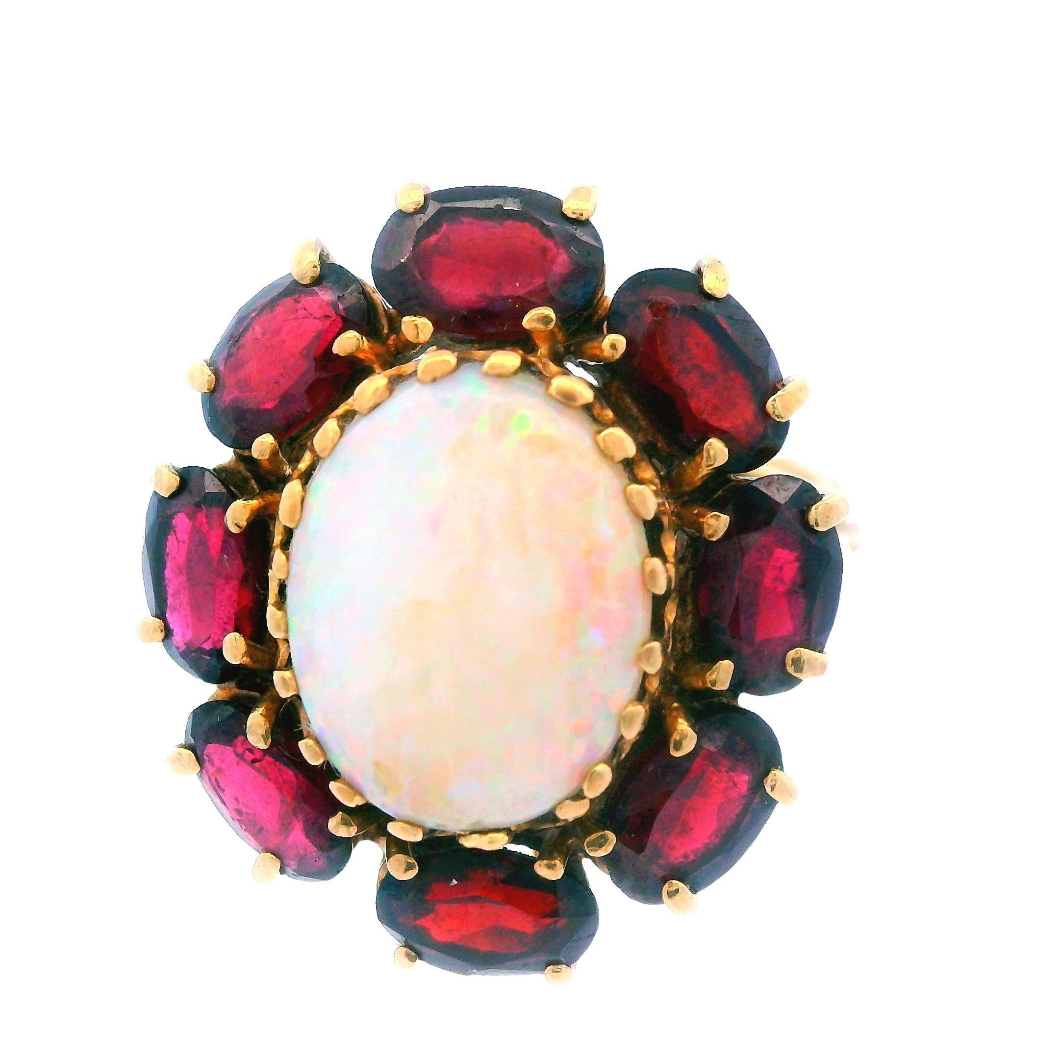 This beautiful opal and red garnet ring is a 1950's design. The ring is 14 karat yellow gold with a white opal centerpiece (12.75x9.55mm opal). The opal has excellent bright red and green flashes with a smooth and even color play. Said opal is