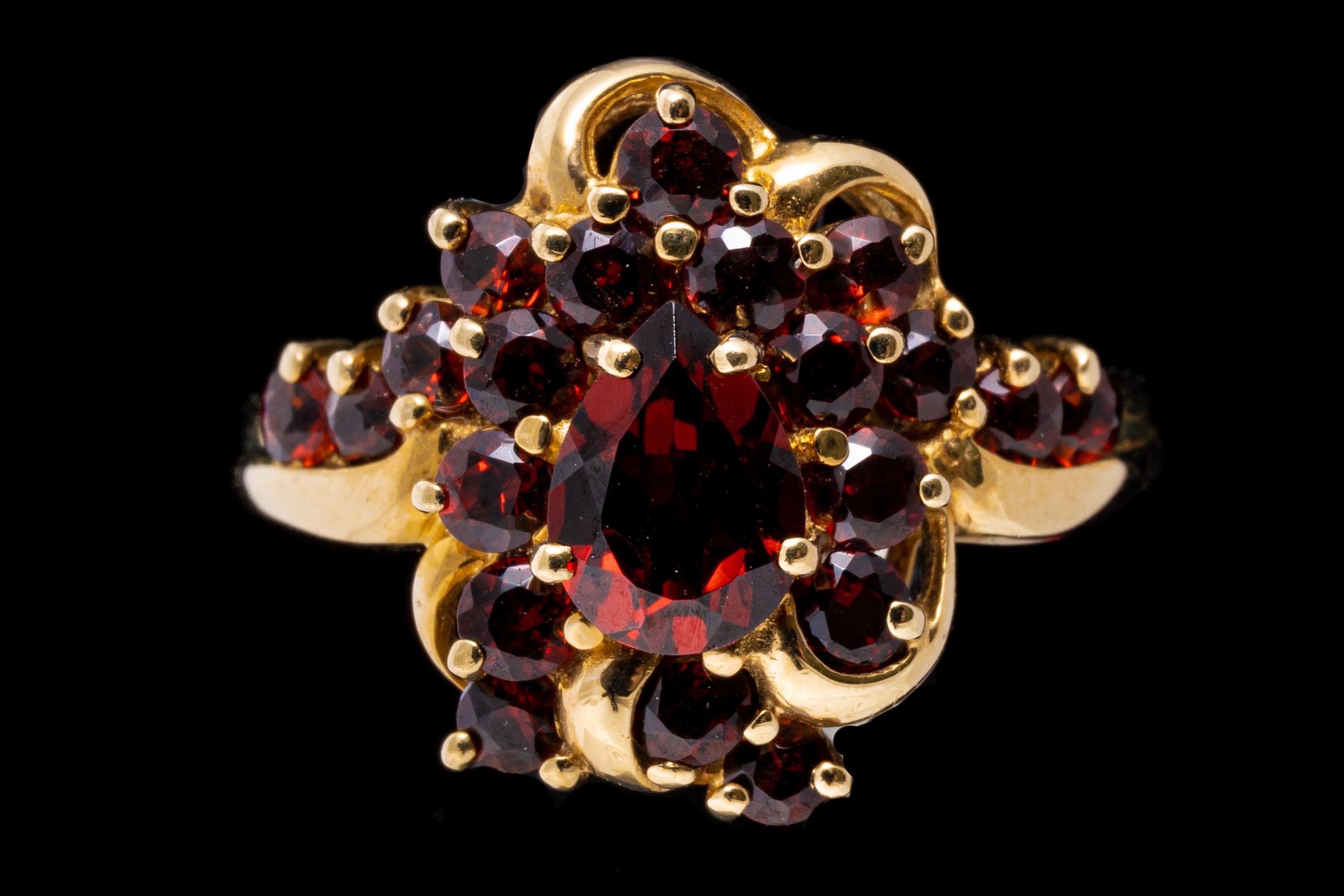 14k yellow gold ring. 14k yellow gold ornate almandine garnet cluster ring, set with a center pear shaped faceted, burgundy color garnet, approximately 0.45 CTS, surrounded by a swirled halo of round faceted garnets, approximately 1.14 TCW, which