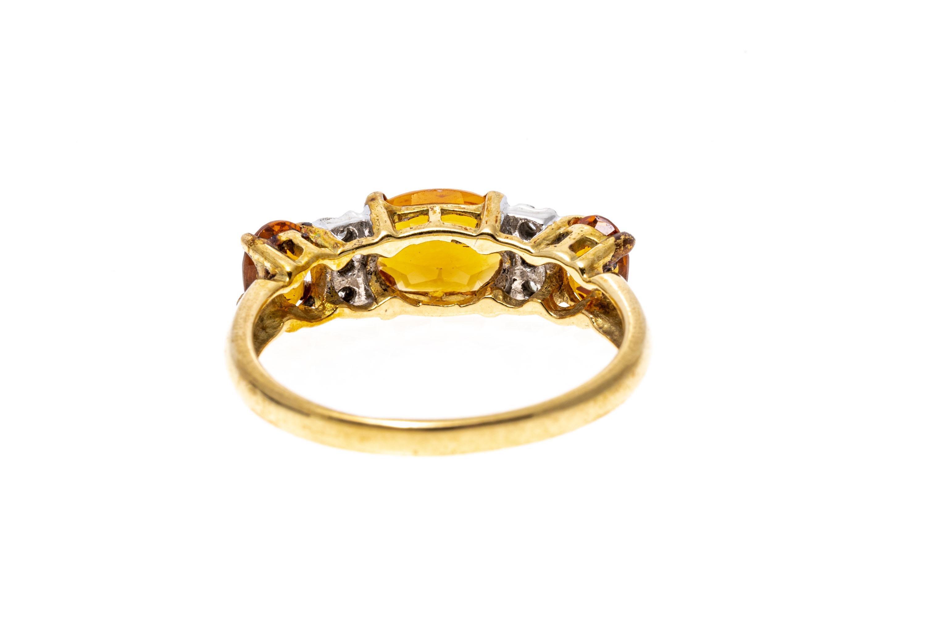 14k yellow gold ring. This attractive ring is a three stone band, featuring a center horiztonal oval and two vertical oval faceted, medium orange color citrines, approximately 1.26 TCW, separated by stacked round faceted accent diamonds,