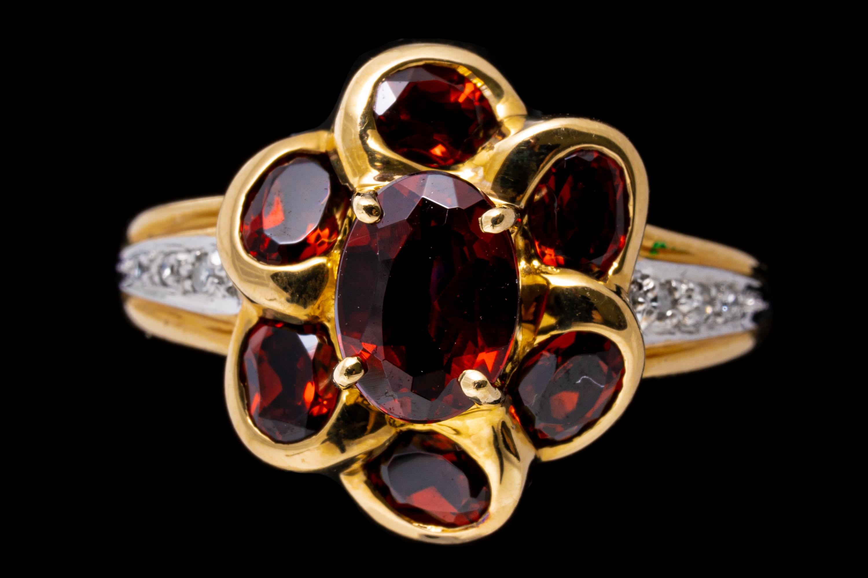 14k yellow gold ring. This lovely flower cluster ring features an oval faceted, burgundy garnet center, approximately 0.55 TCW, prong set, surrounded by petals of oval faceted, burgundy color garnets, approximately 0.54 TCW. The center is flanked