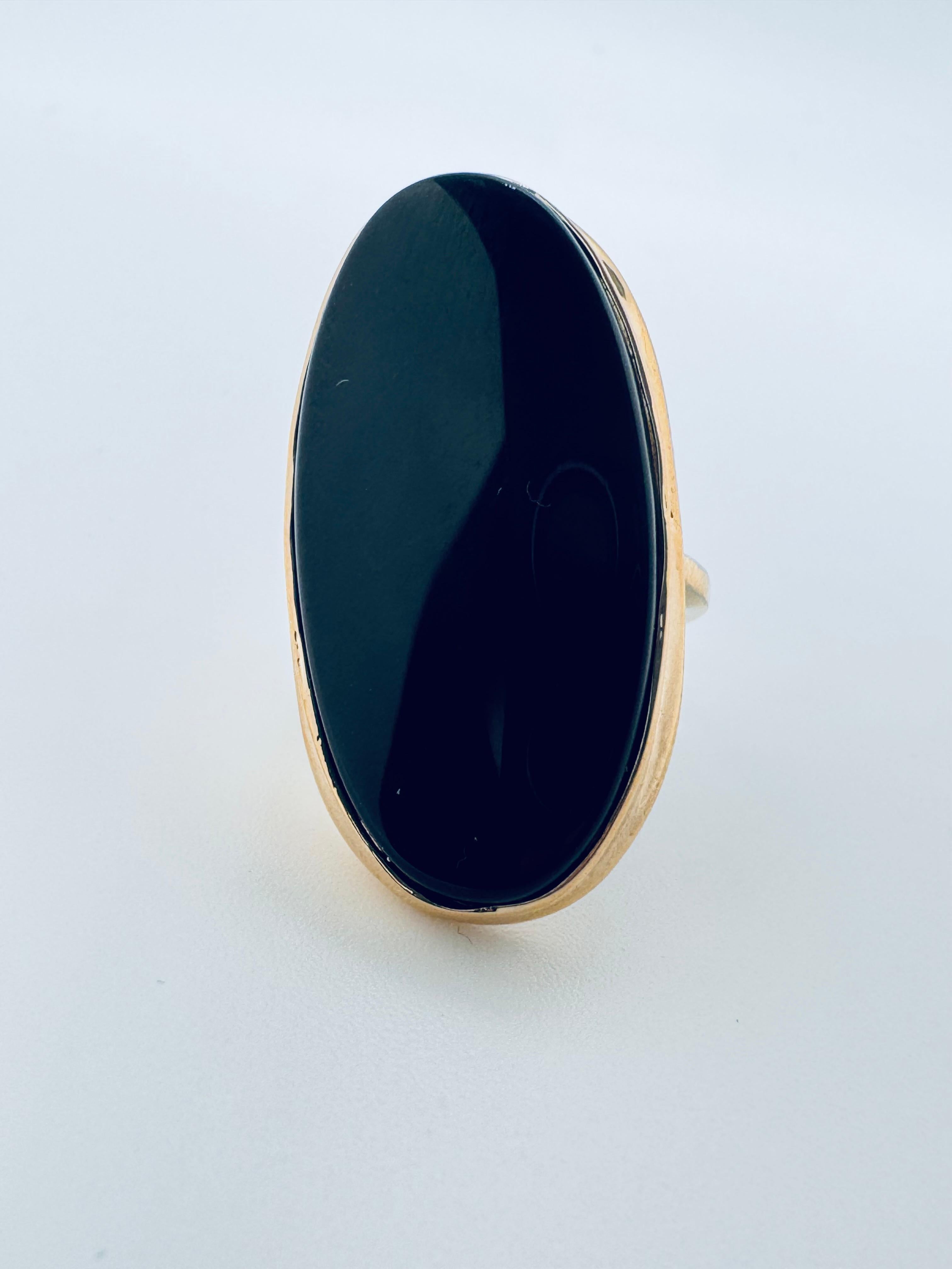 Cette bague en or jaune 14 carats est ornée d'un grand onyx ovale mesurant environ 29,7 mm sur 15 mm, ce qui en fait une pièce de choix. L'onyx noir, lisse et poli, contraste magnifiquement avec la chaude monture en or jaune, créant un look