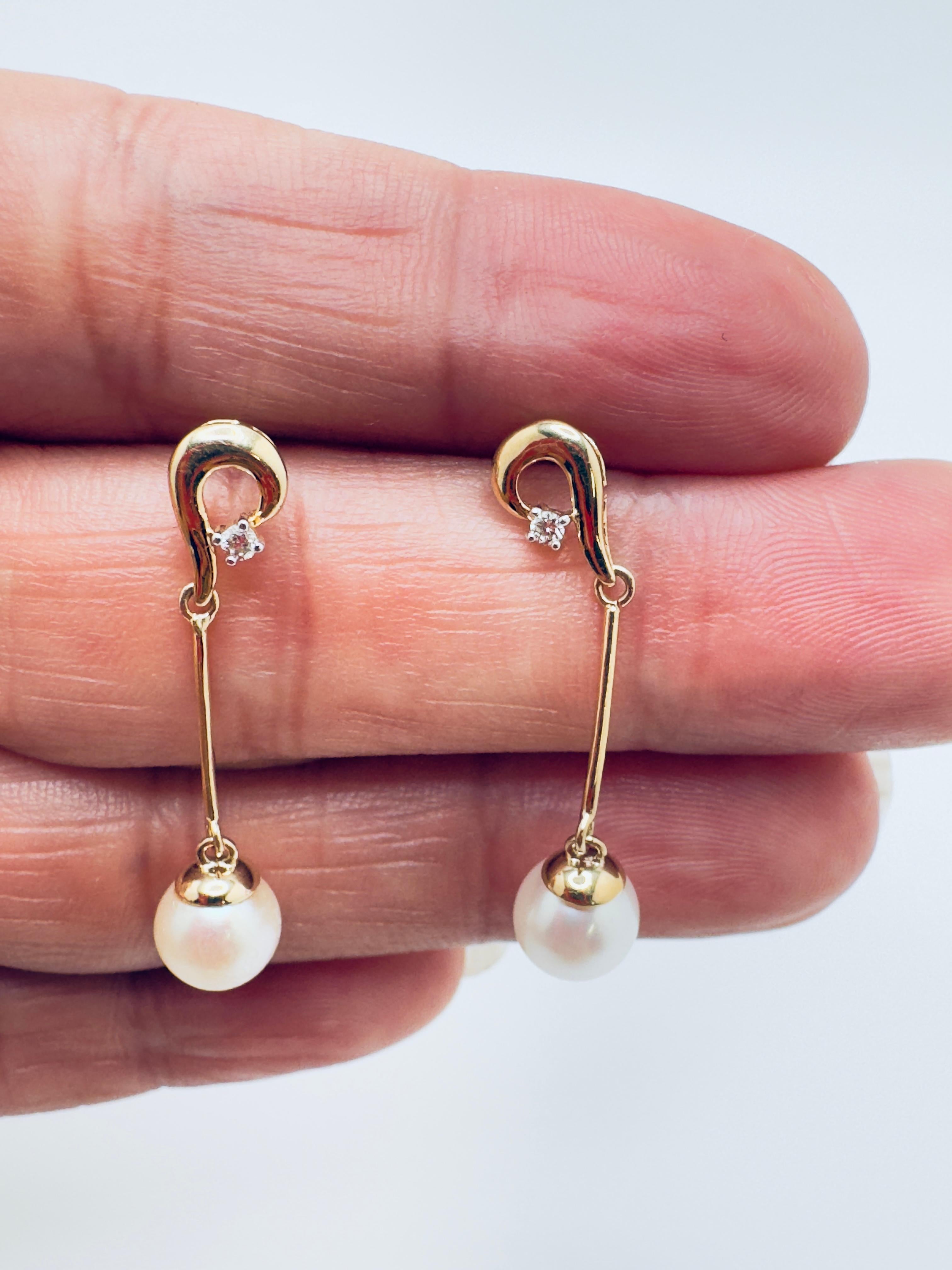 These elegant 14K yellow gold dangle earrings combine the classic beauty of pearls with the sparkling brilliance of diamonds. Each earring features a lustrous white alloy pearl, fully drilled to allow graceful movement, enhancing its natural shine