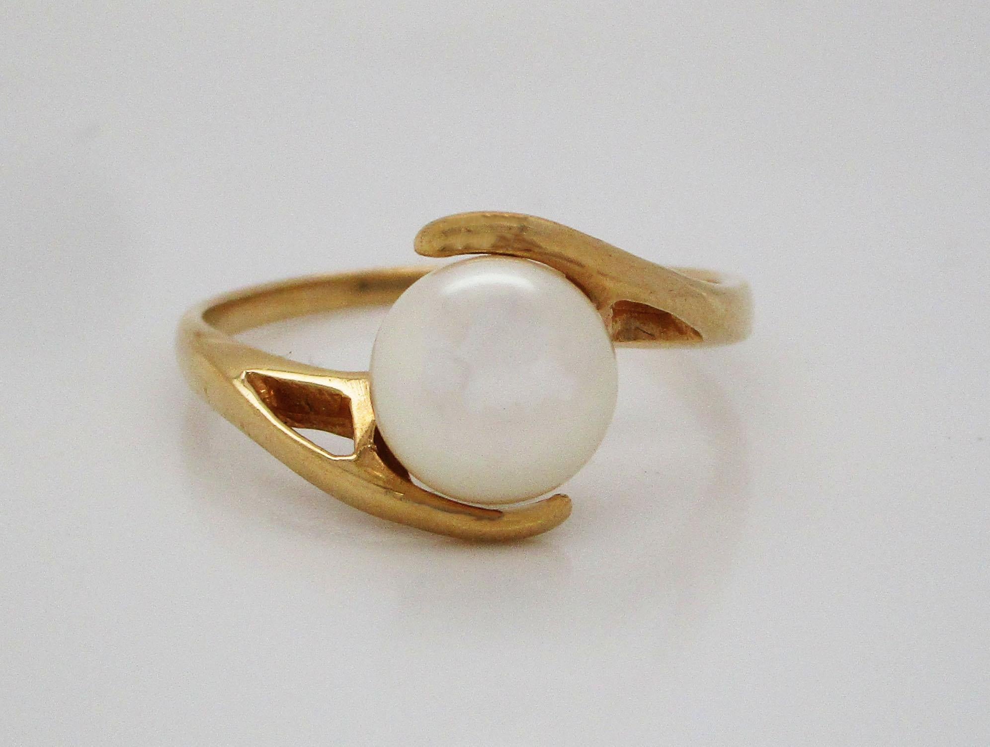This stunning ring is in 14k yellow gold in a beautiful bypass design and boasting a gorgeous white pearl center! This is the ideal ring for someone searching for a non-traditional engagement ring. The pairing of 14k yellow gold and the brilliant
