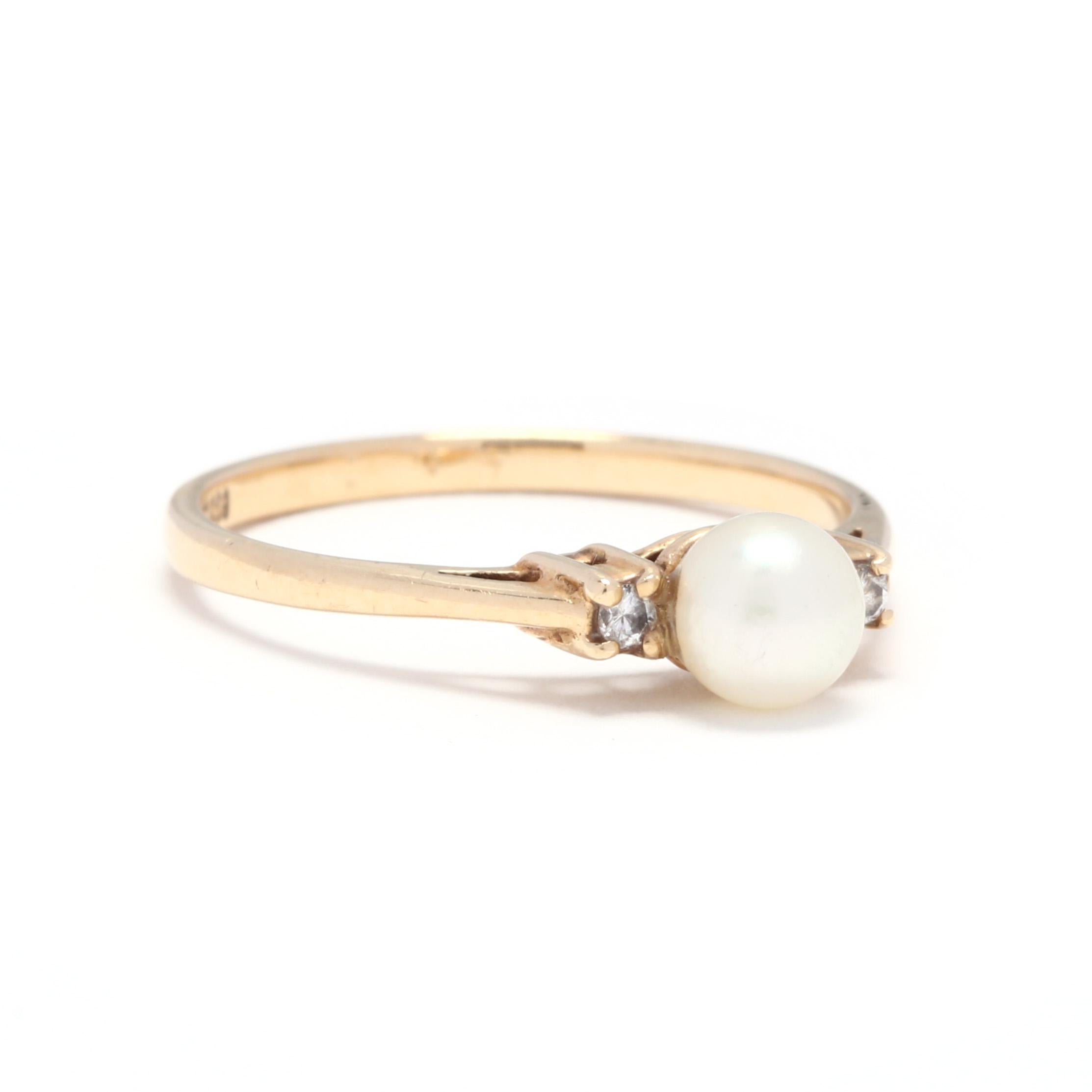 A 14 karat yellow gold, pearl and diamond three stone ring. This ring features a round bead, white pearl center stone with a full cut round diamond on either side and a slightly tapered shank.

Stones:
- pearl
- round bead, 1 stone
- 5.1 mm

-